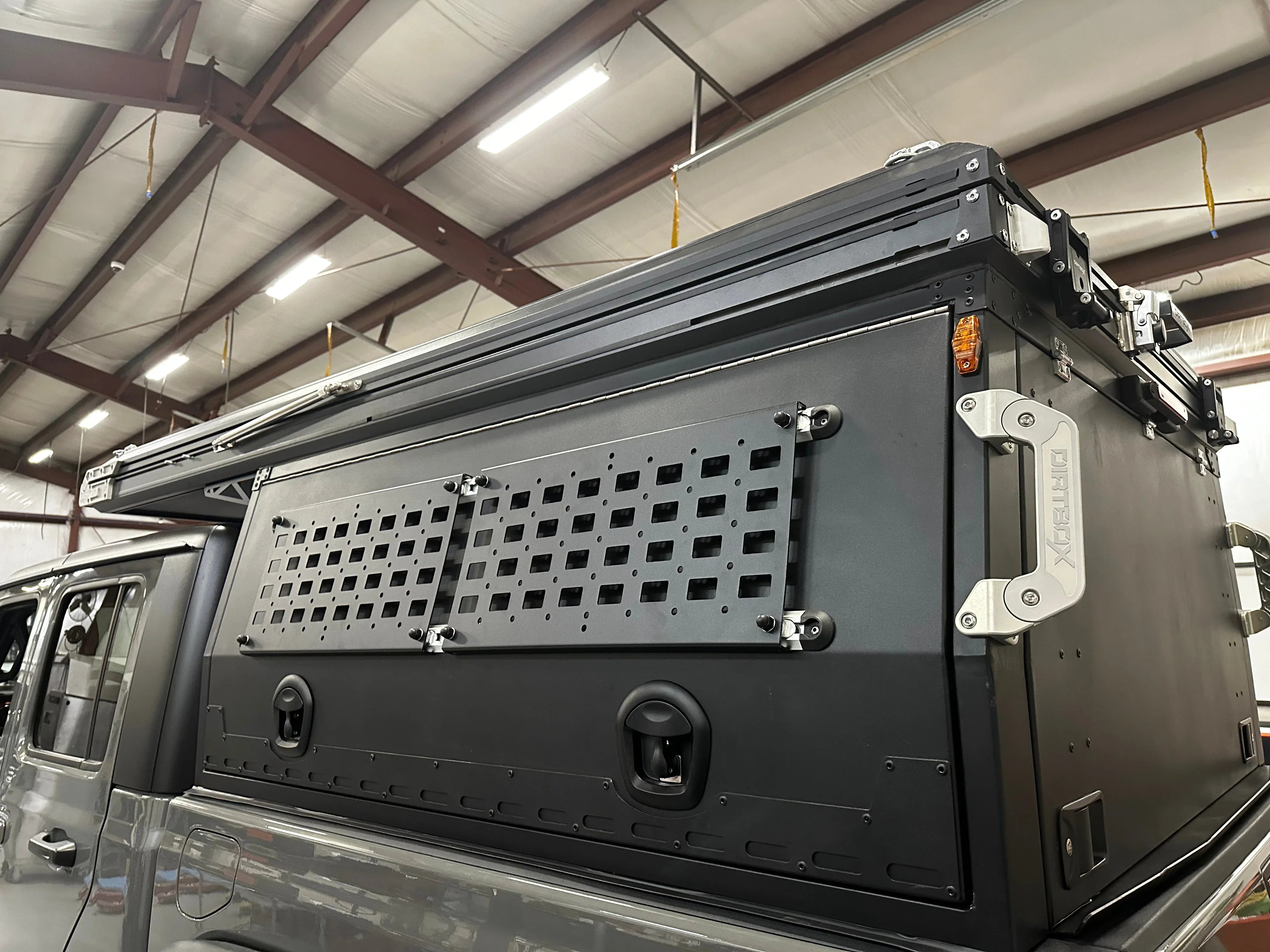 Overland truck bed camper canopy with modular storage panels and awning in a garage