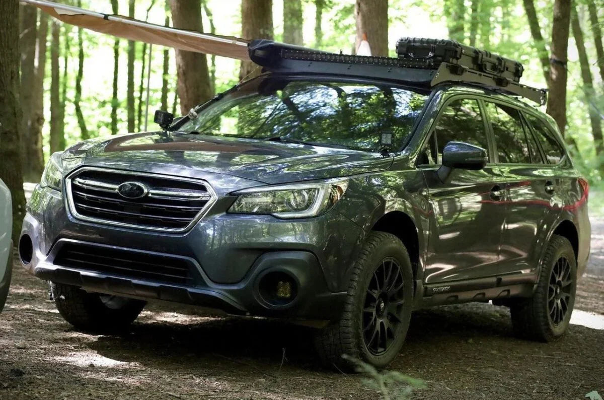 Overland-ready Subaru SUV with roof rack, awning extended, parked in forest campsite