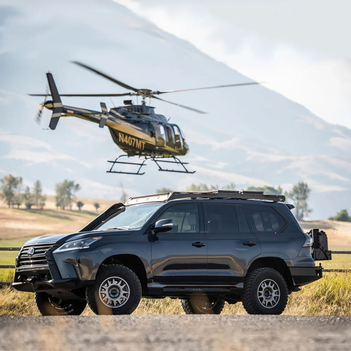 Off-road SUV with roof rack and rugged tires in outdoor adventure setting, helicopter in background