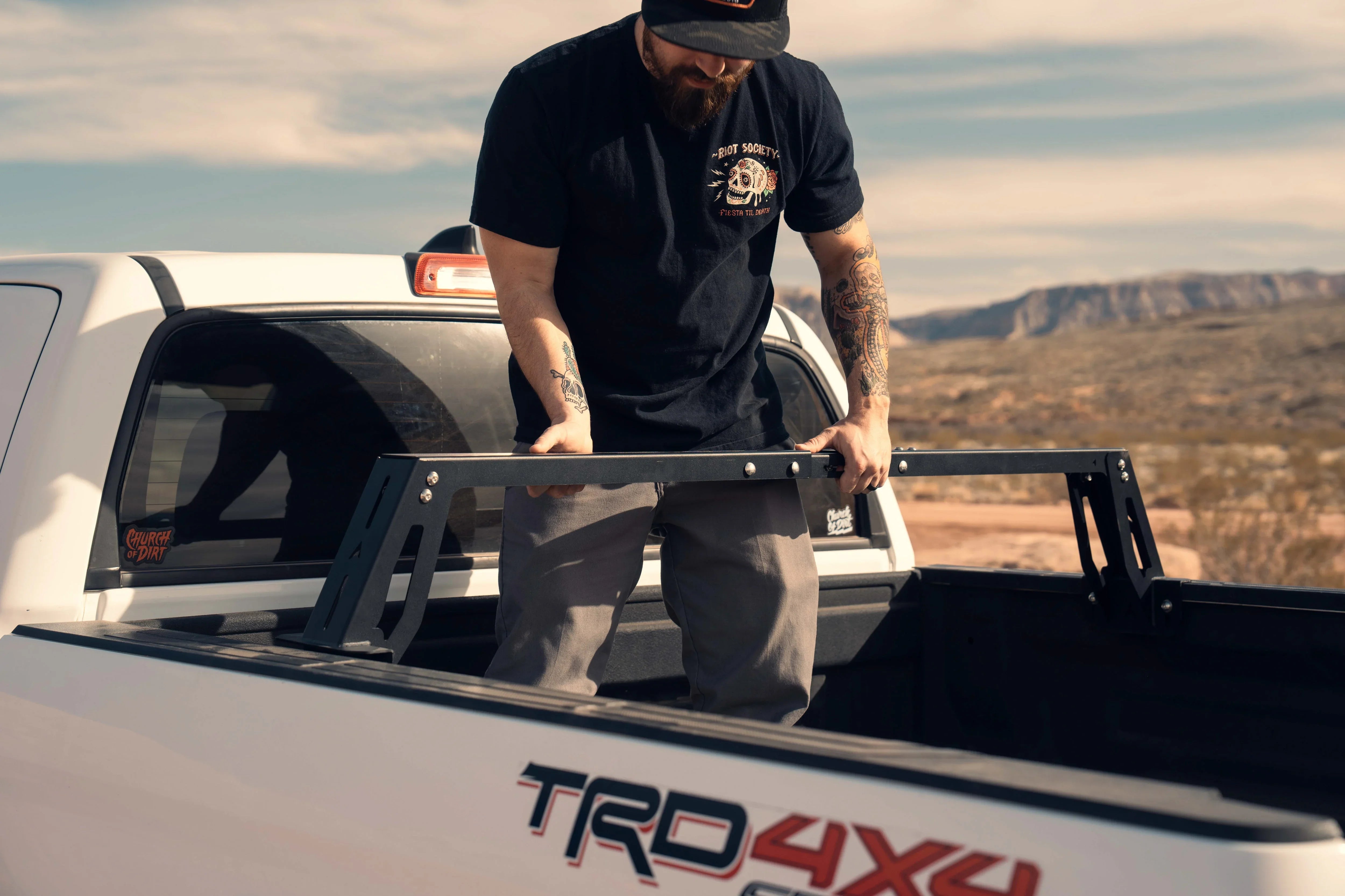 Man installs a modular bed rack in a Toyota Tacoma TRD 4x4 truck outdoors
