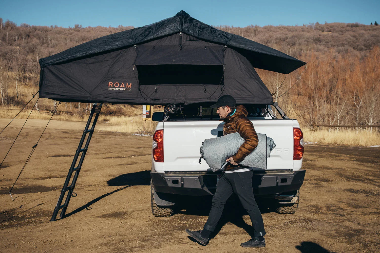Man unloading bedding from pickup truck with rooftop tent for overlanding camping