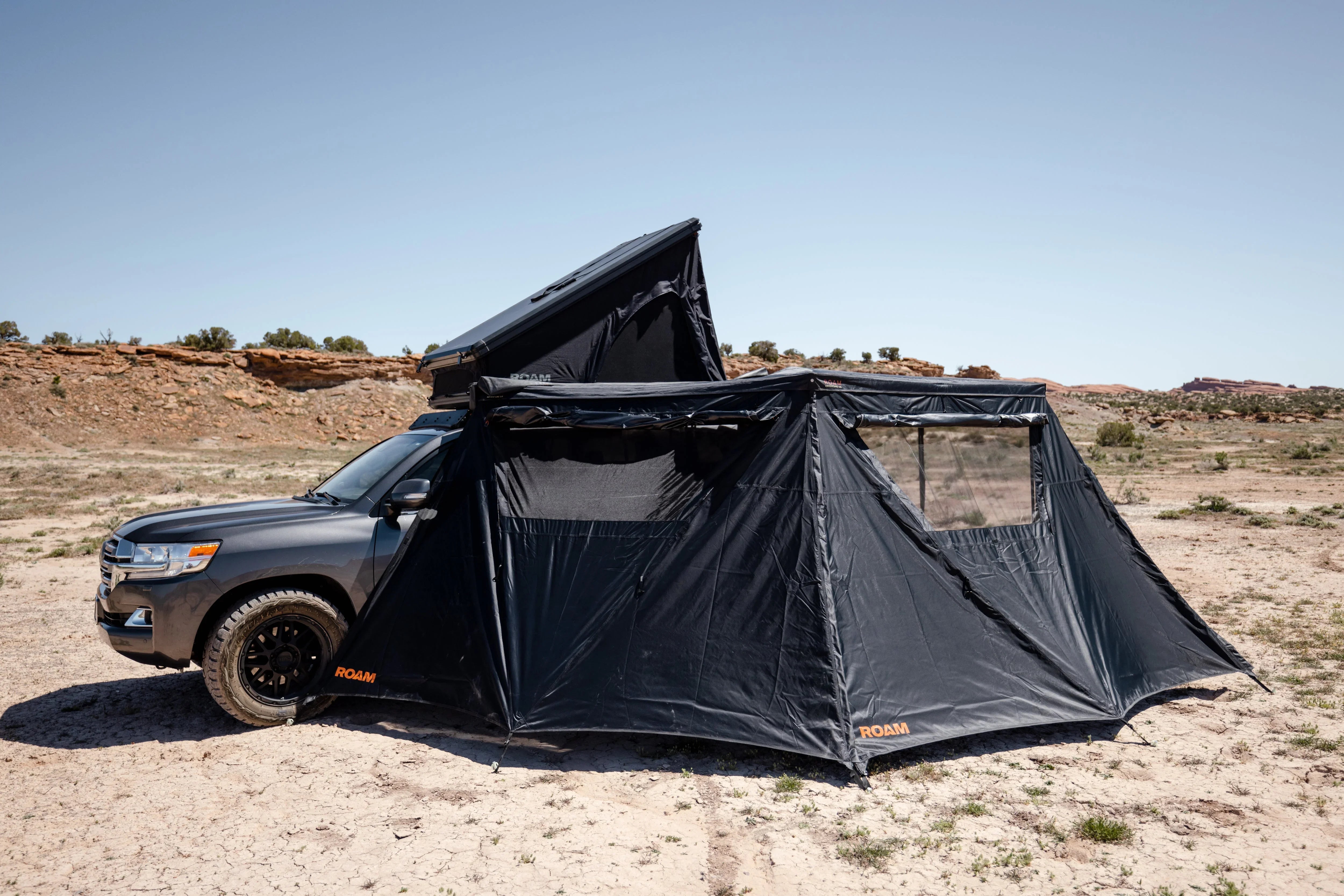 Overland vehicle with rooftop tent and annex set up in desert landscape