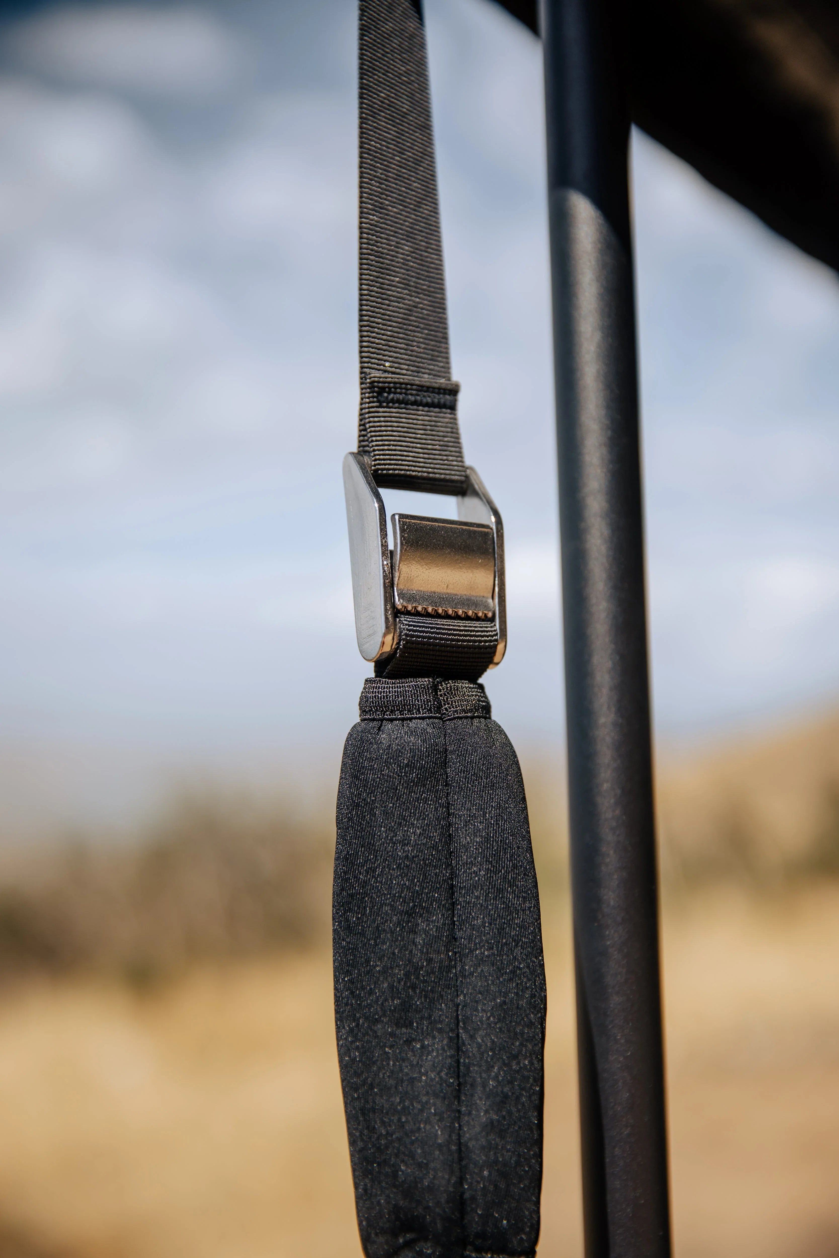 Close-up of black overland gear strap with metal buckle, outdoor adventure background