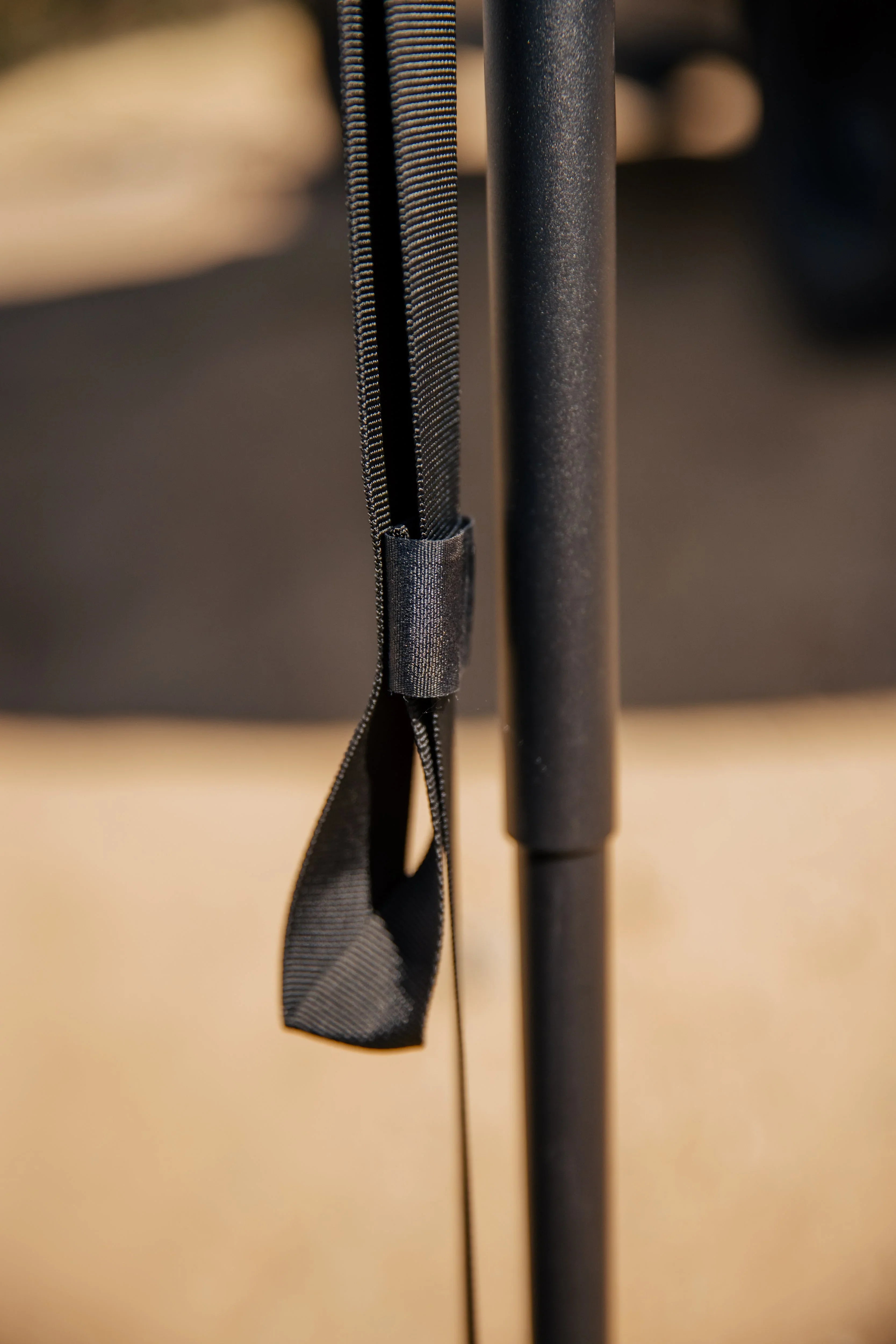 Close-up of a black nylon strap loop on a metal camping gear pole outdoors
