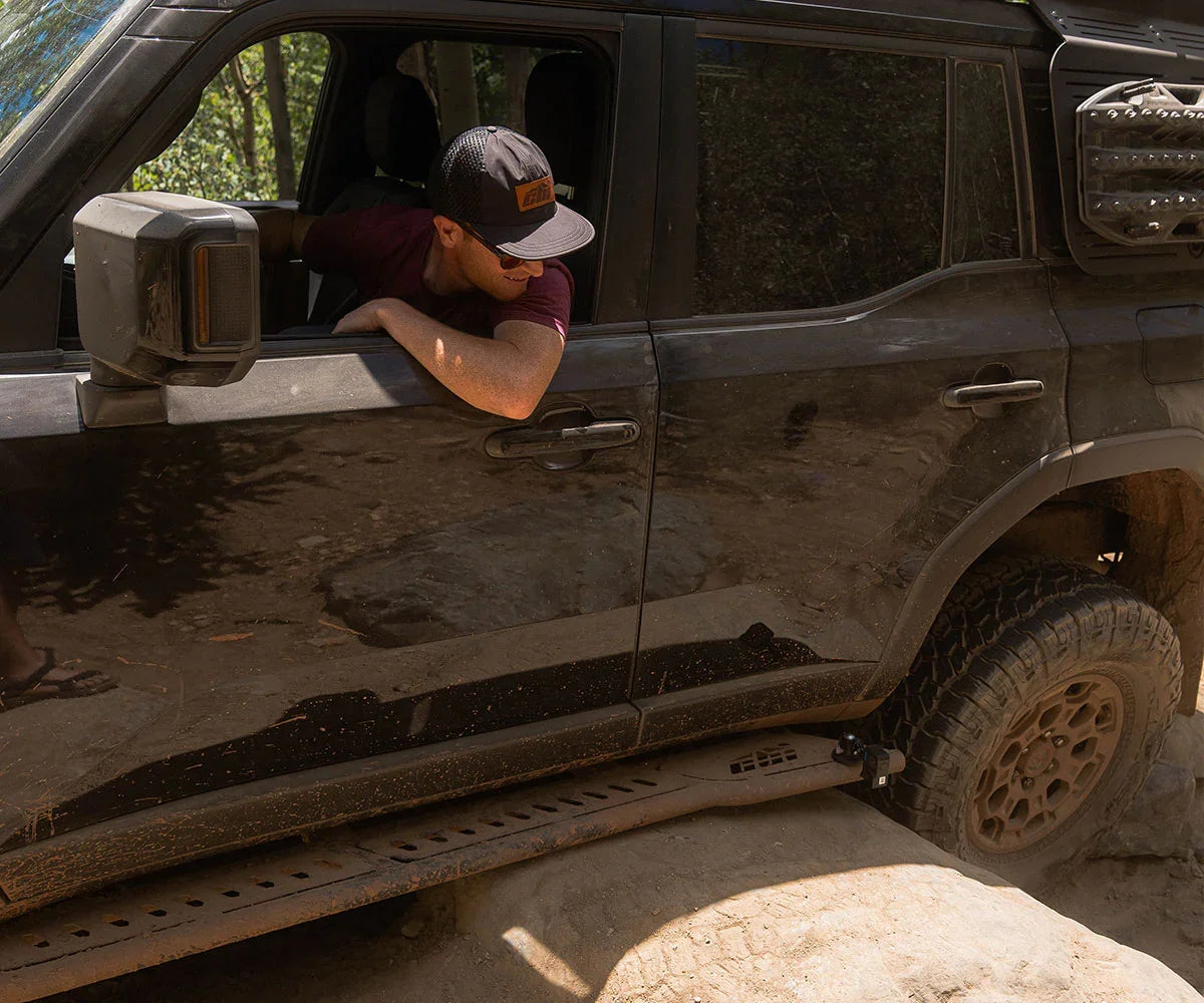 Man driving off-road SUV over rocky terrain with expedition rock sliders and mud tires