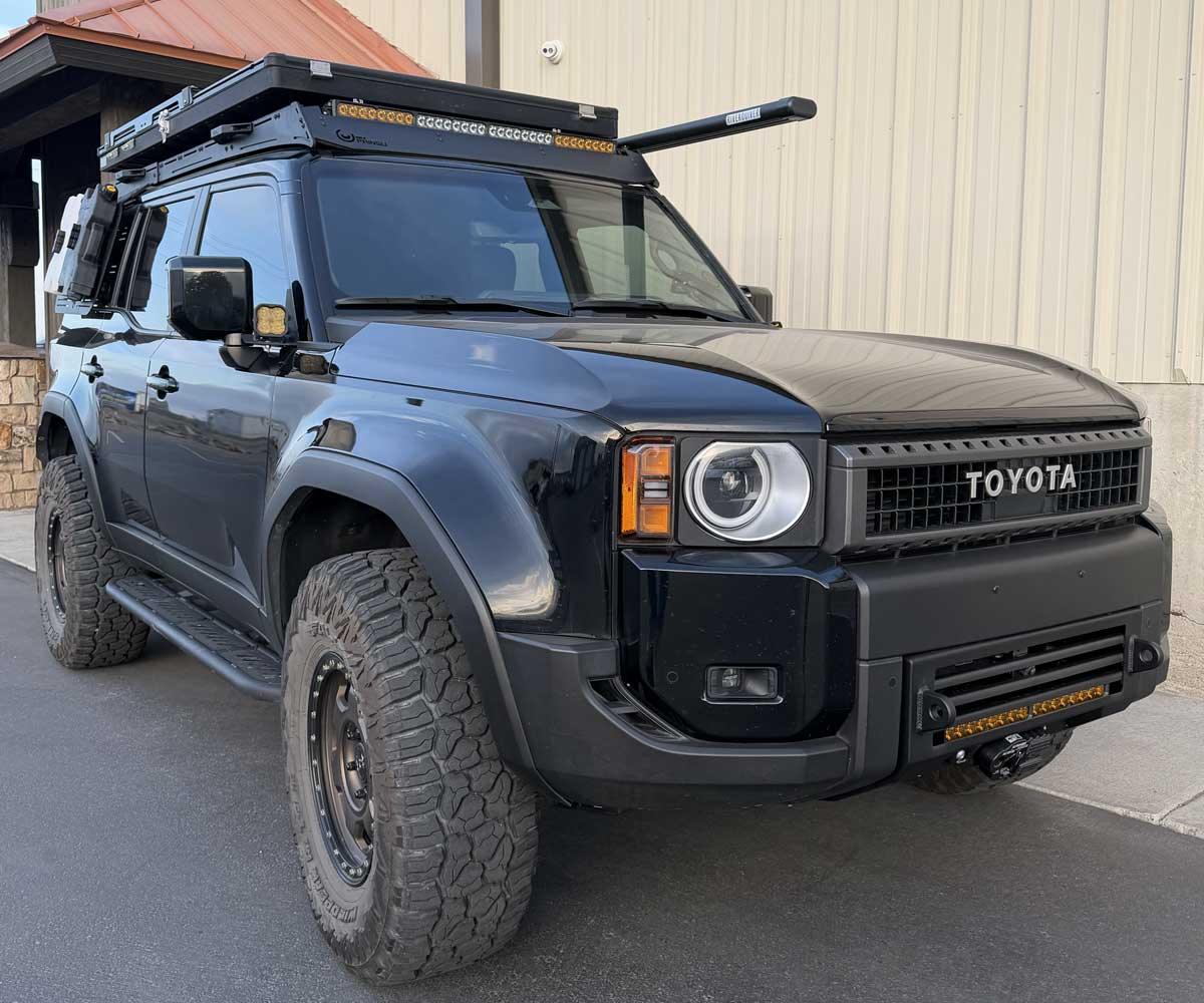 Black Toyota off-road SUV with roof rack and camping gear, parked outdoors