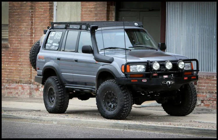Toyota Land Cruiser with off-road roof rack, lift kit, and expedition accessories parked by brick wall