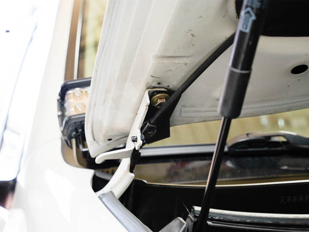 Close-up of installed ditch light bracket under white vehicle hood, overland accessory