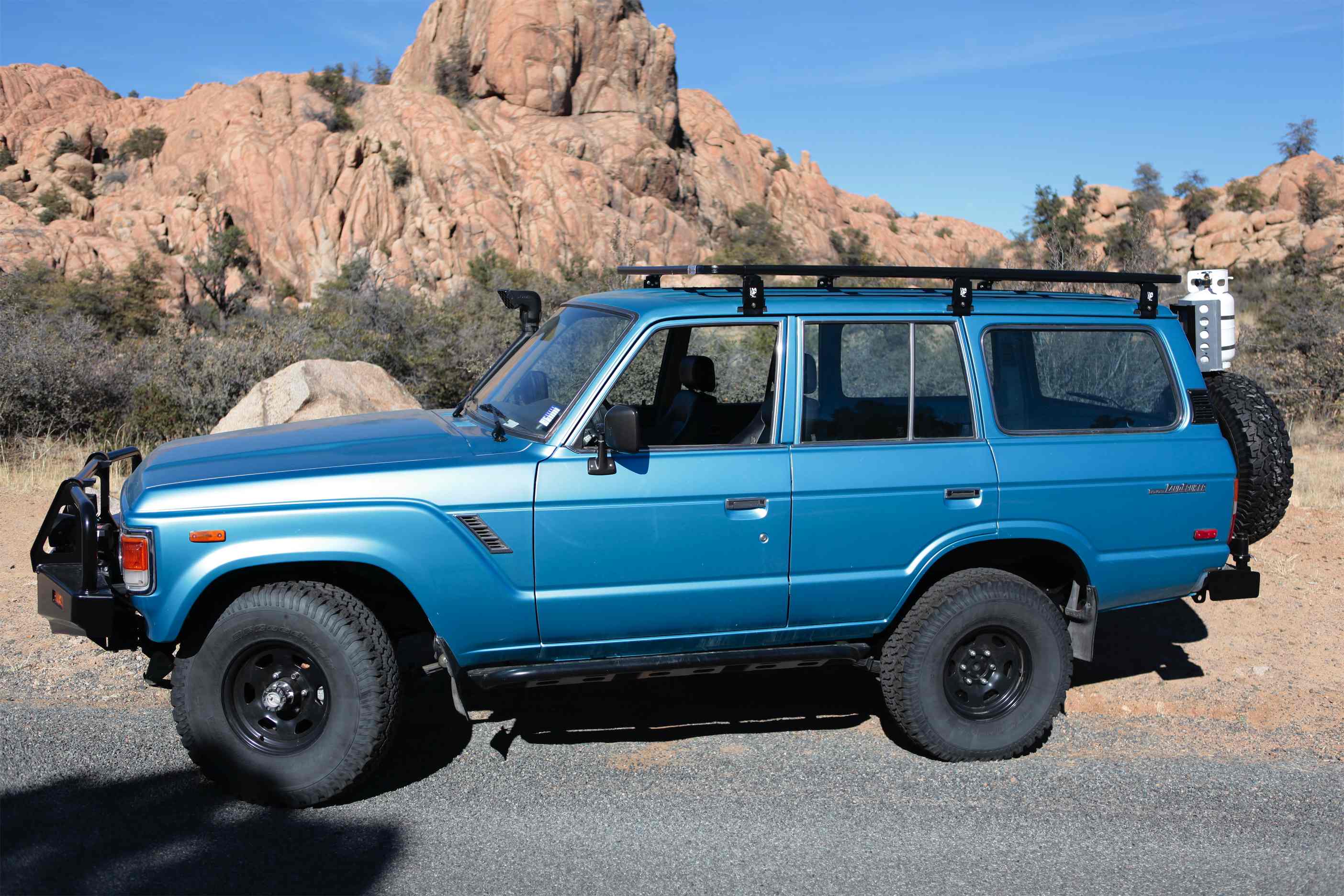 Blue overland SUV with off-road tires and roof rack parked in desert terrain