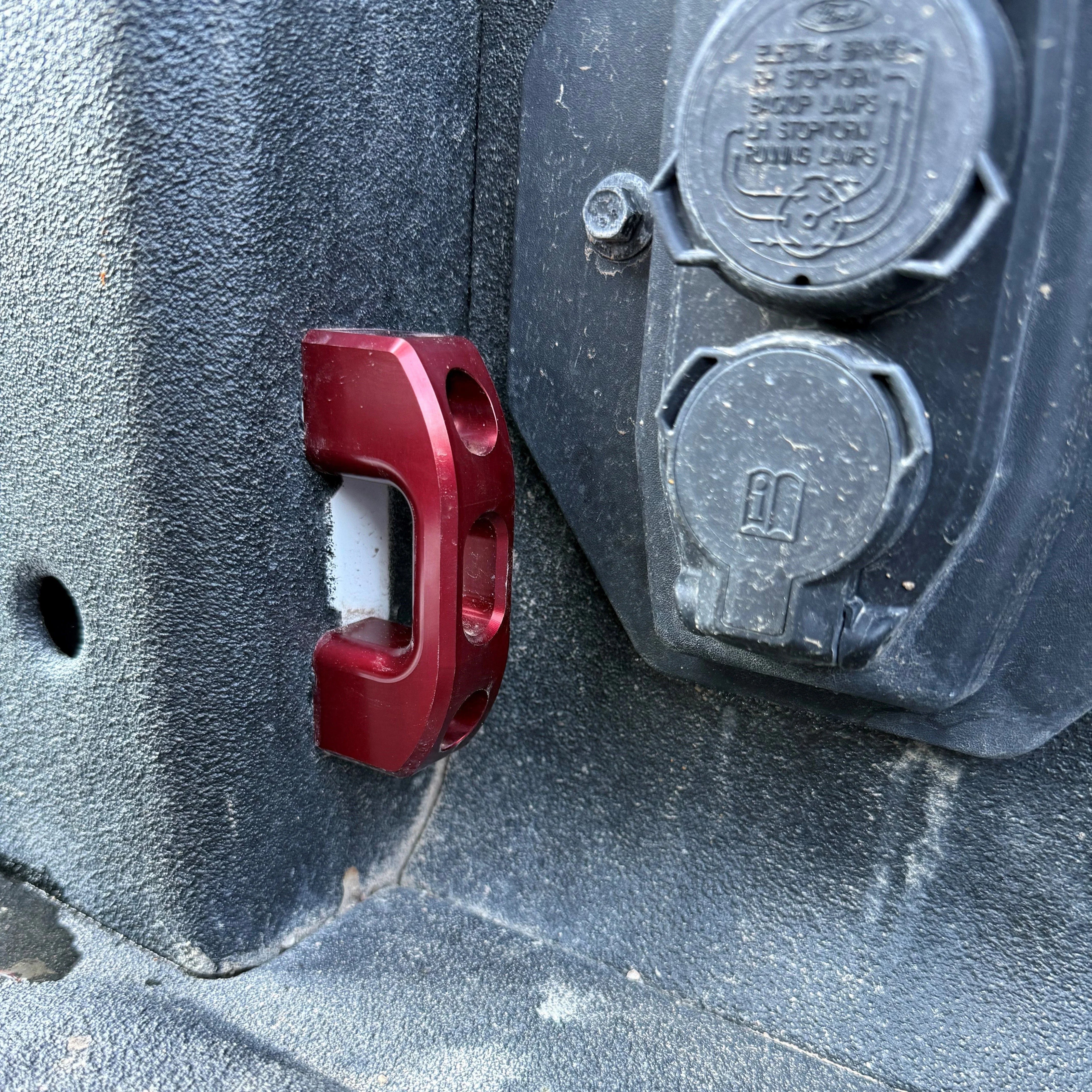 Red aluminum bed tie-down anchor and trailer plug on truck bed liner