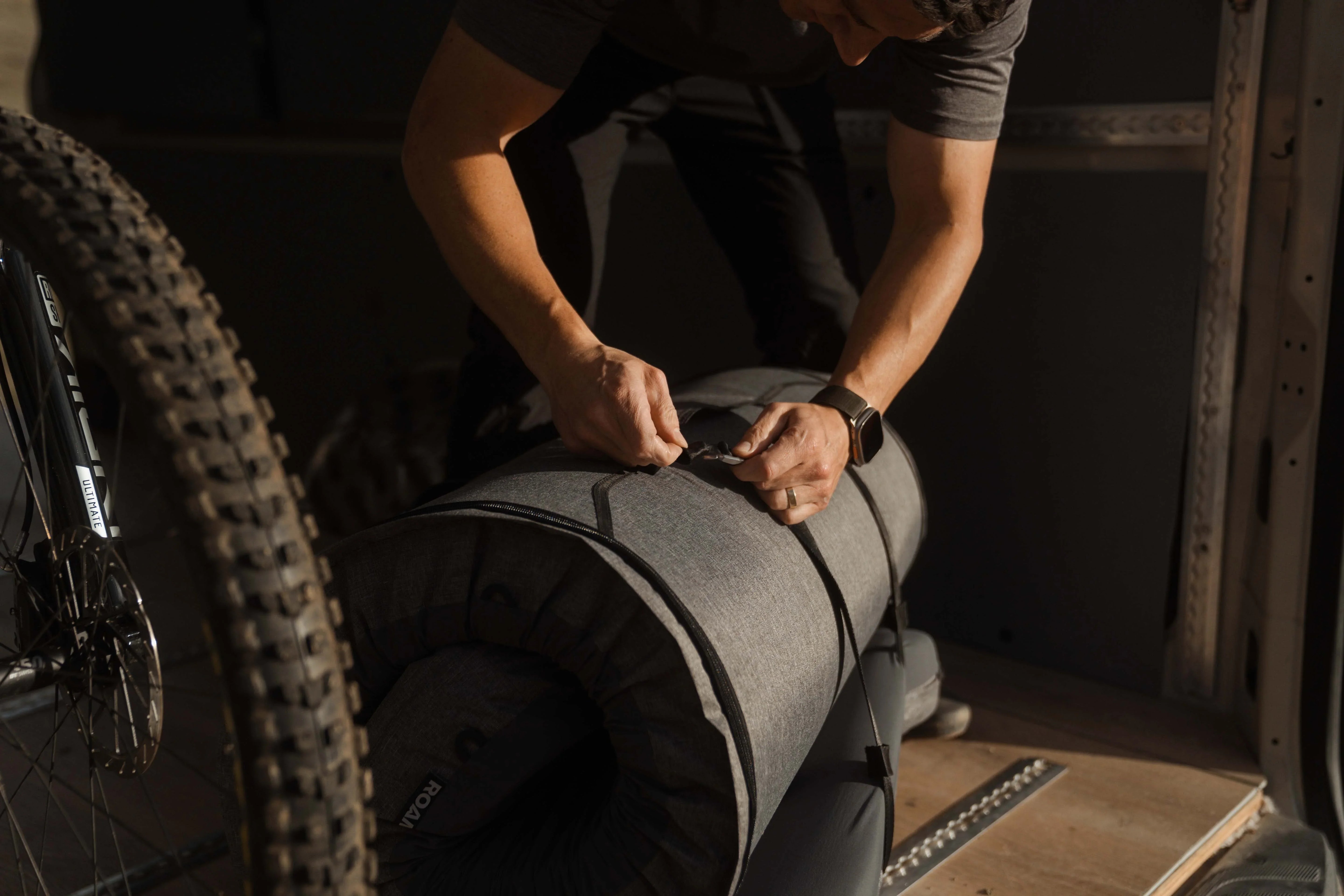Person securing a rolled-up camping mattress inside a vehicle next to a mountain bike tire.