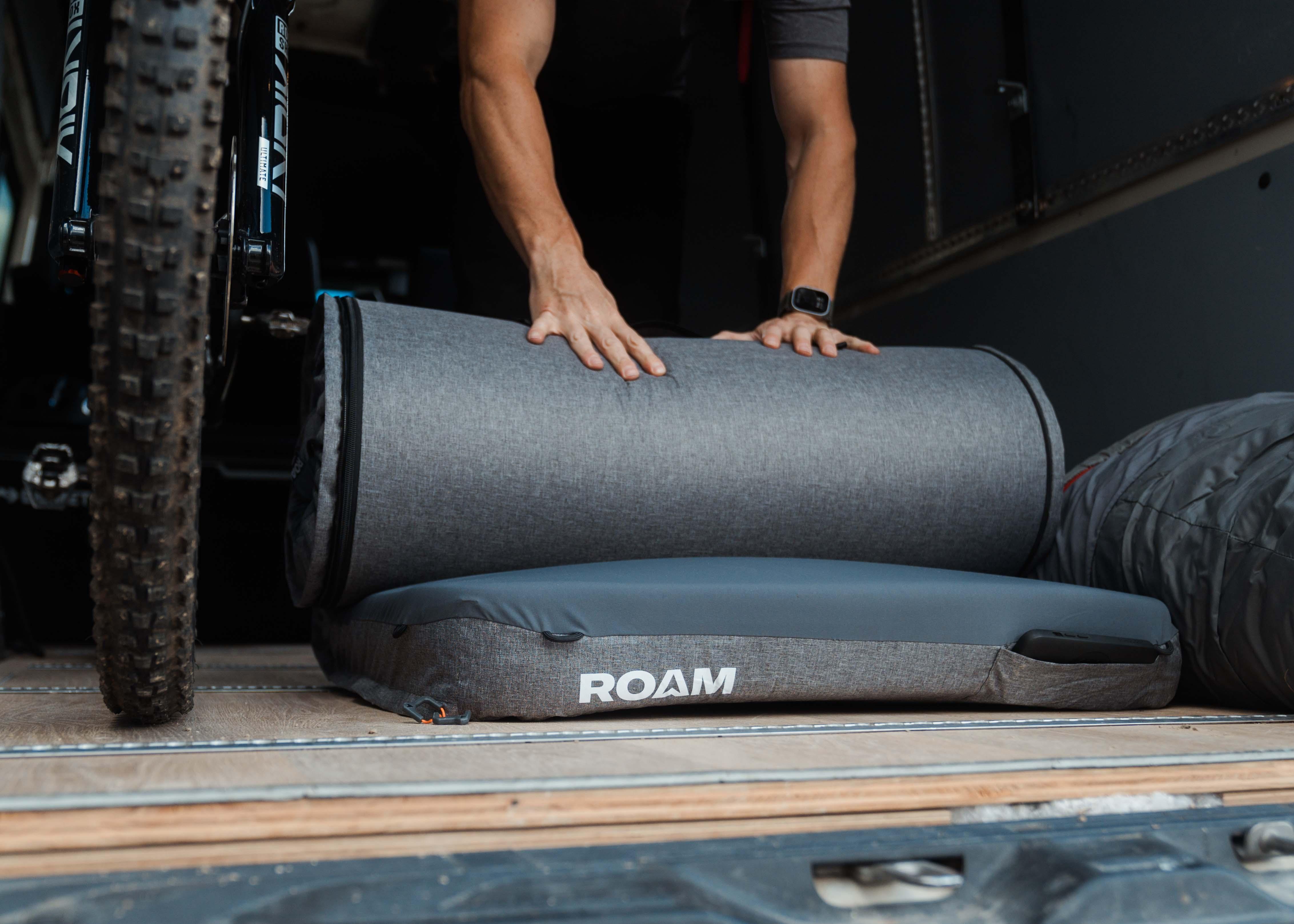 Rolling up a ROAM camping mattress in a vehicle next to a mountain bike, adventure gear scene