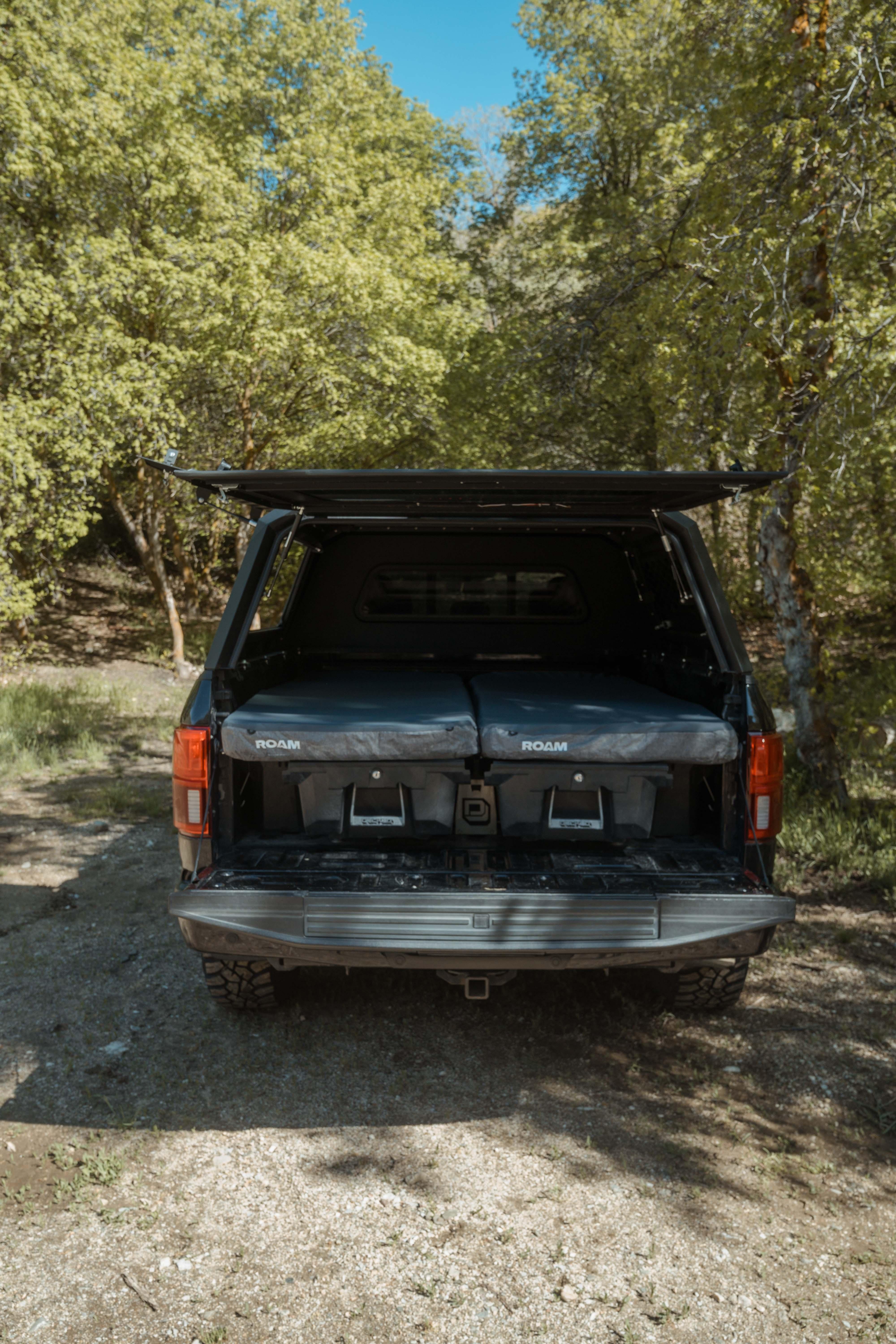 Truck bed with ROAM camping mattress and storage bins, outdoor overlanding setup