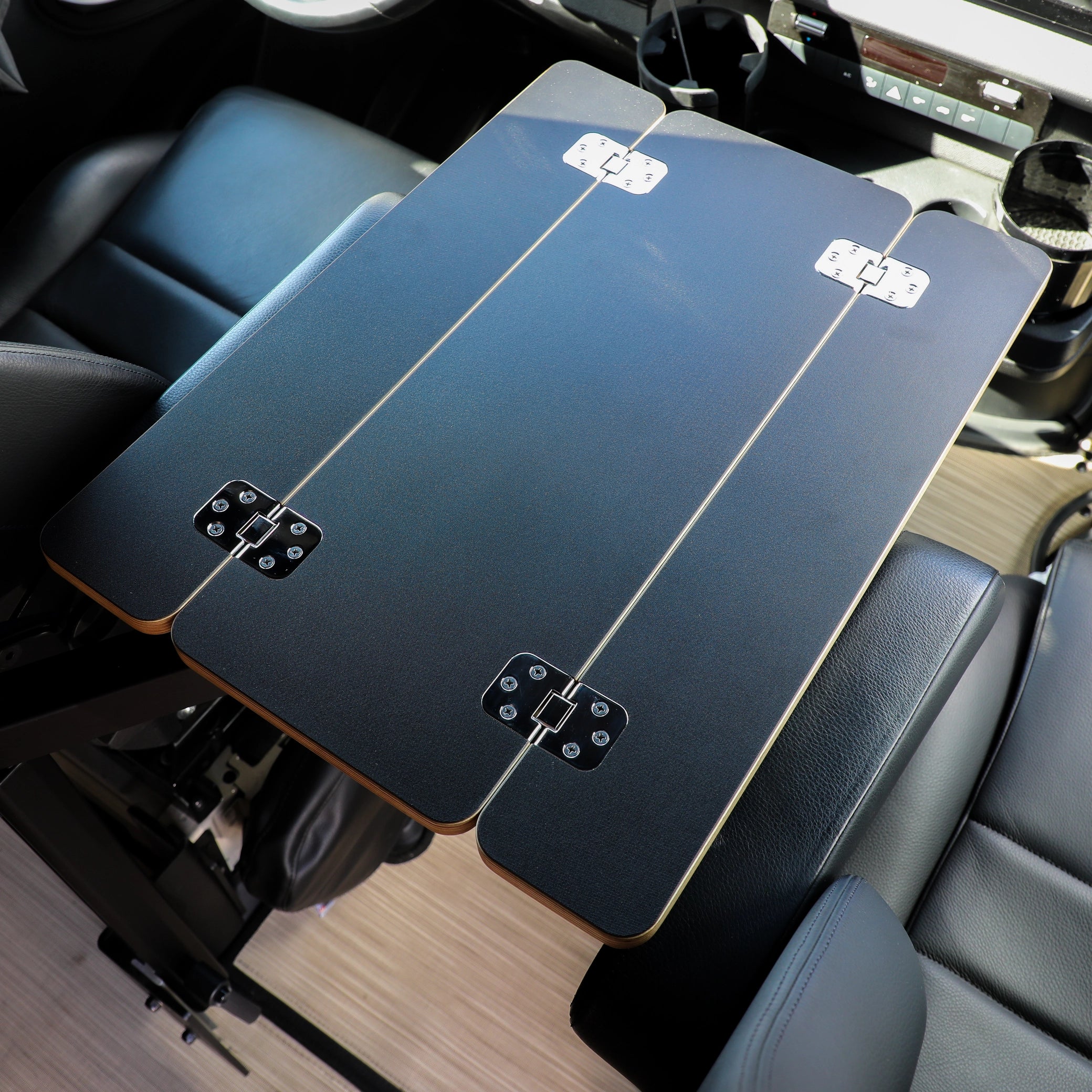 Foldable black vehicle seat-back table for overlanding and camping in a car interior