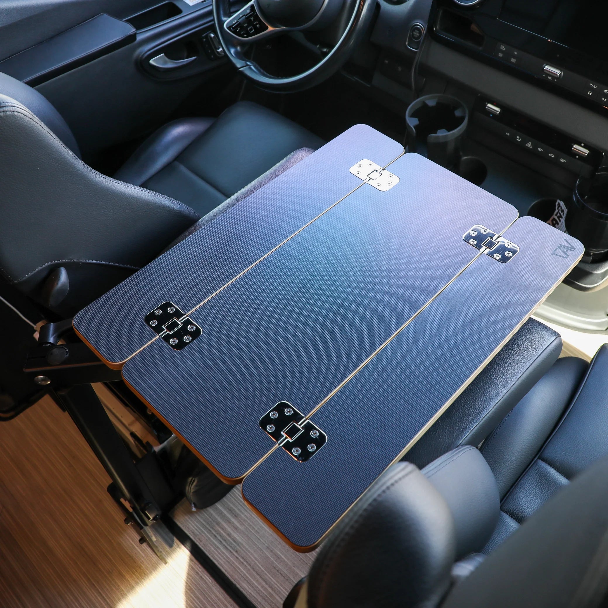 Foldable overland camping table set up inside vehicle between driver and passenger seat.