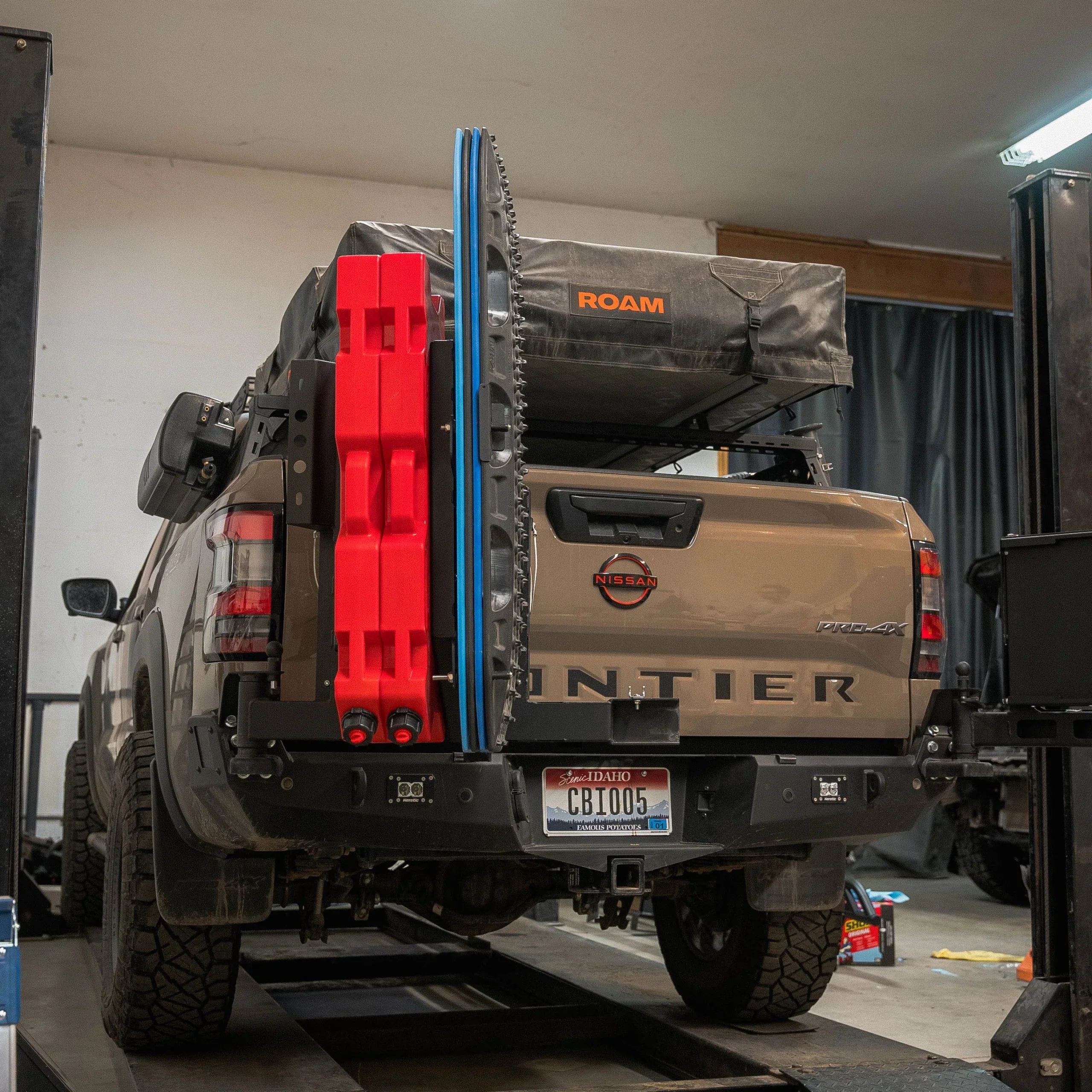 Nissan Frontier with overlanding gear, recovery boards, and roof tent in garage