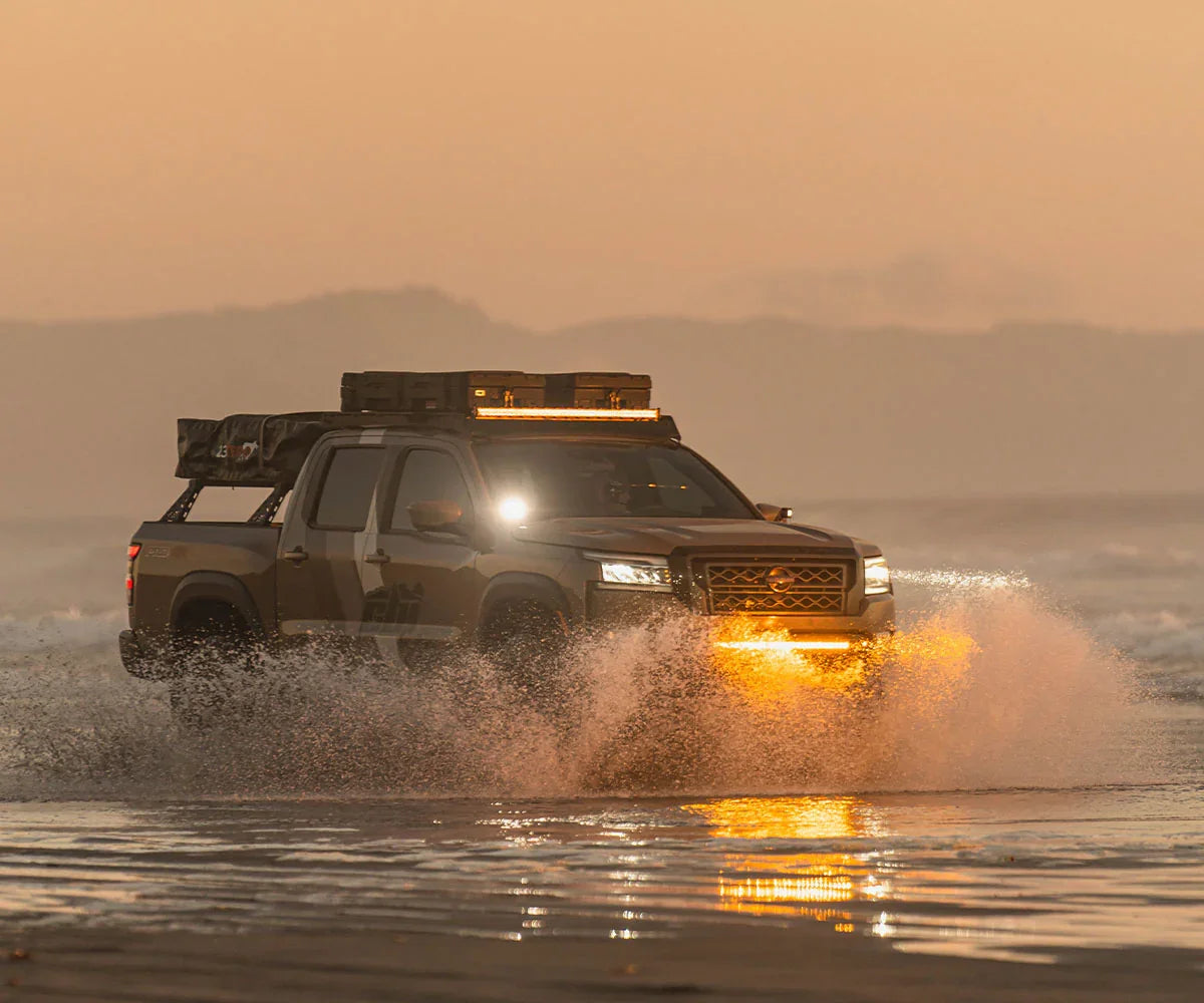 Nissan Frontier overland truck with covert bumper and roof gear driving on beach at sunset
