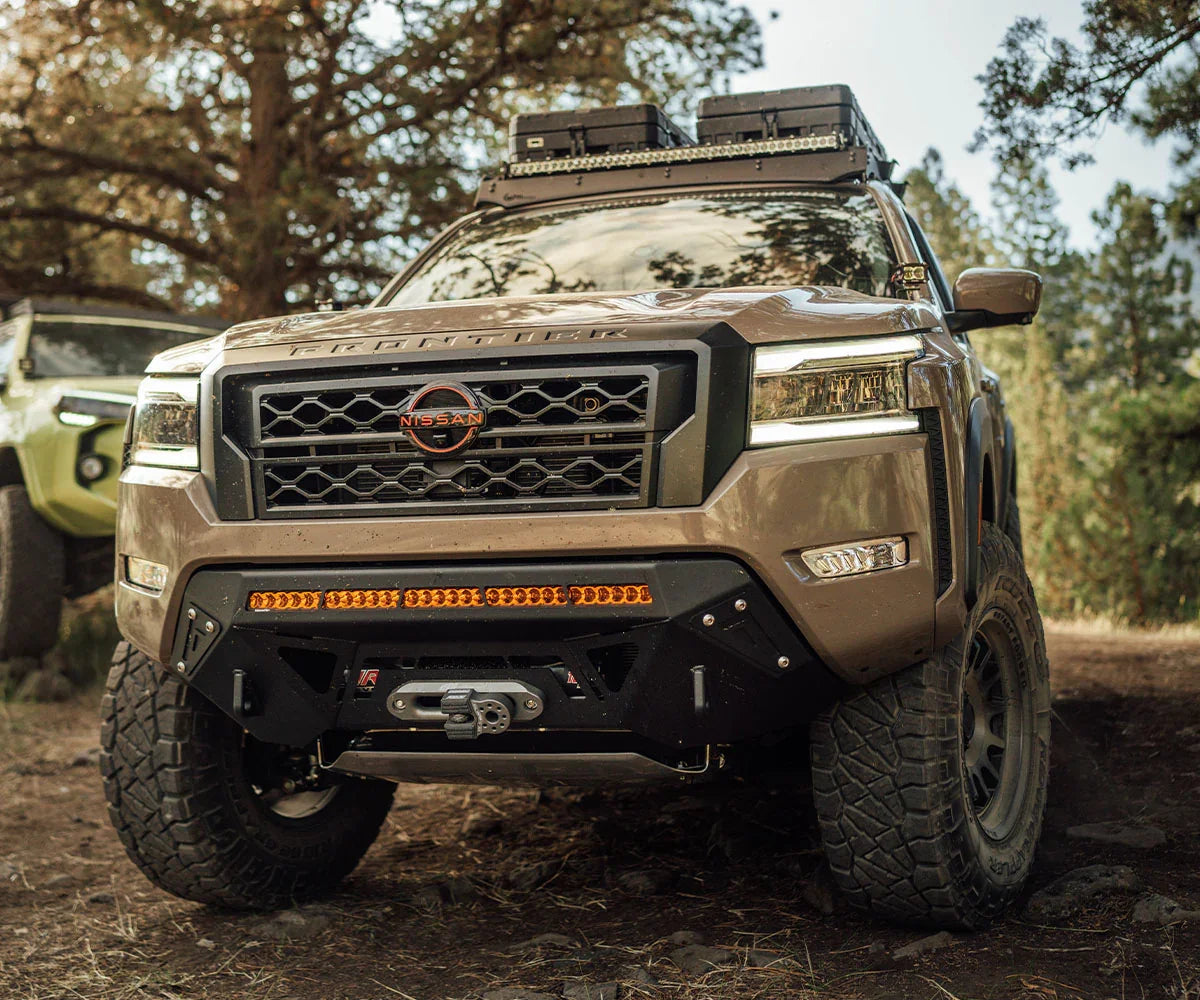 Nissan Frontier overland build with Covert front bumper, off-road tires, and roof gear in forest