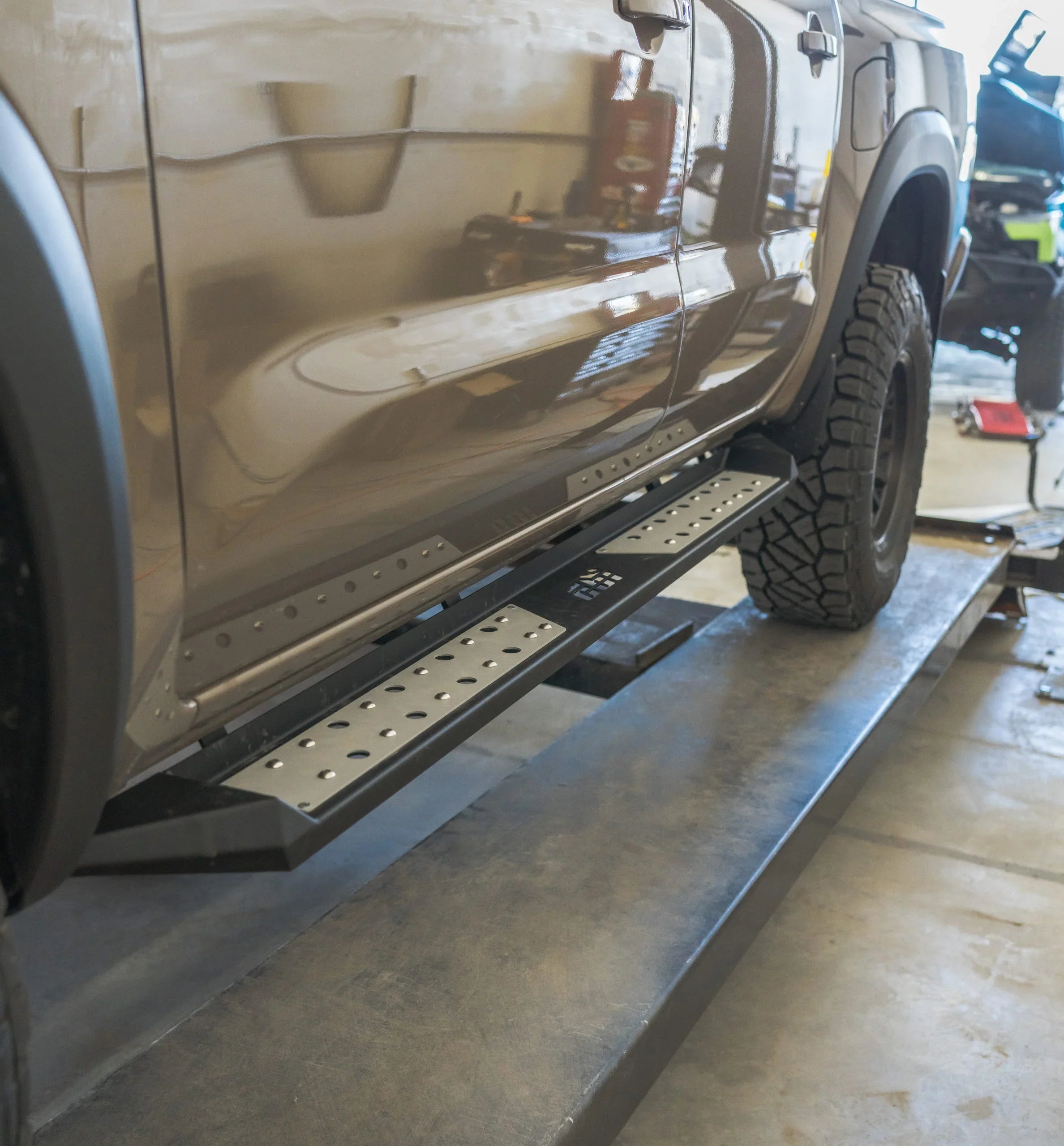 Heavy-duty steel rock slider side step on lifted Nissan truck in garage setting