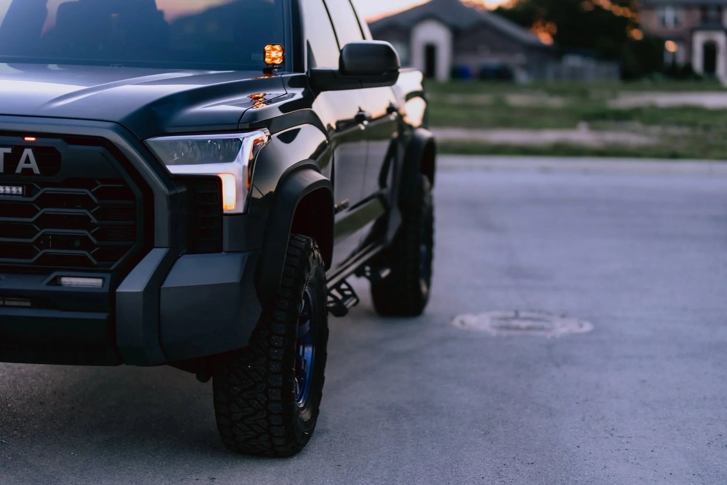 Custom Toyota truck with off-road tires and LED lights parked outdoors at sunset