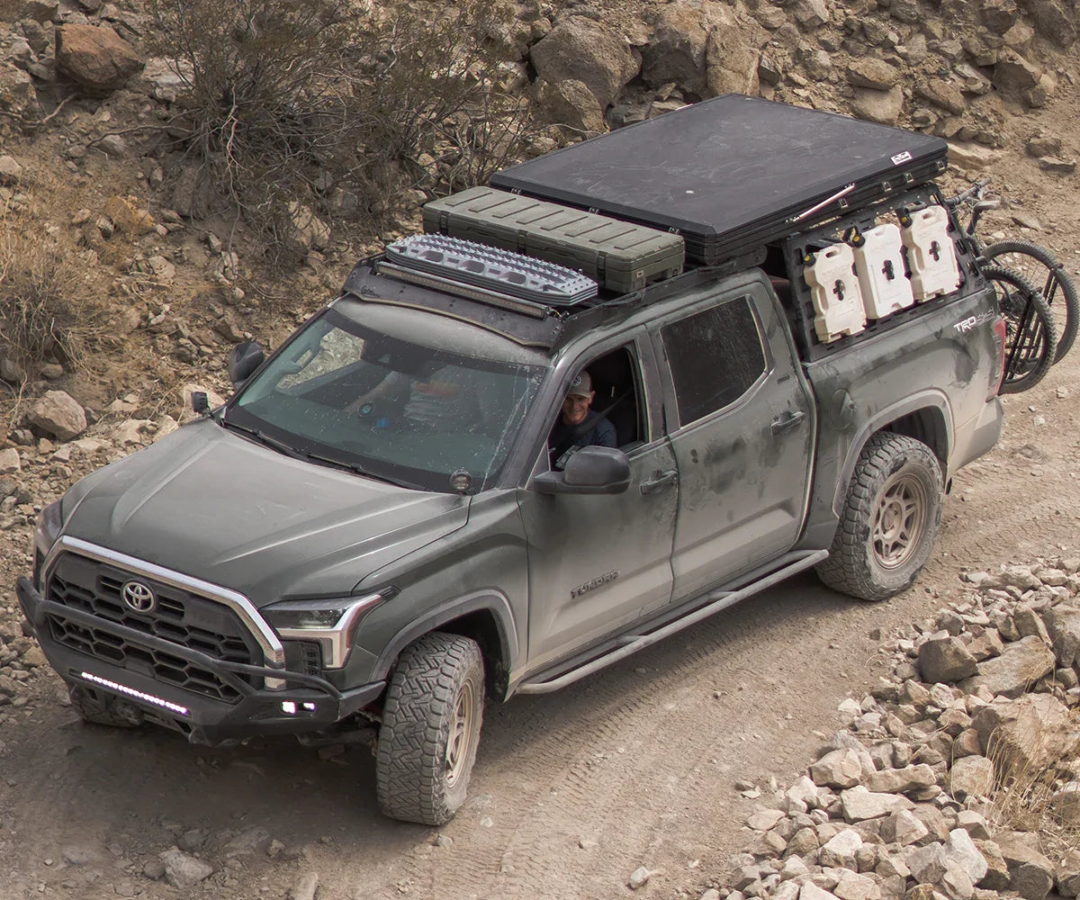 Overland-equipped 2022 Toyota Tundra driving on rocky dirt trail with expedition gear