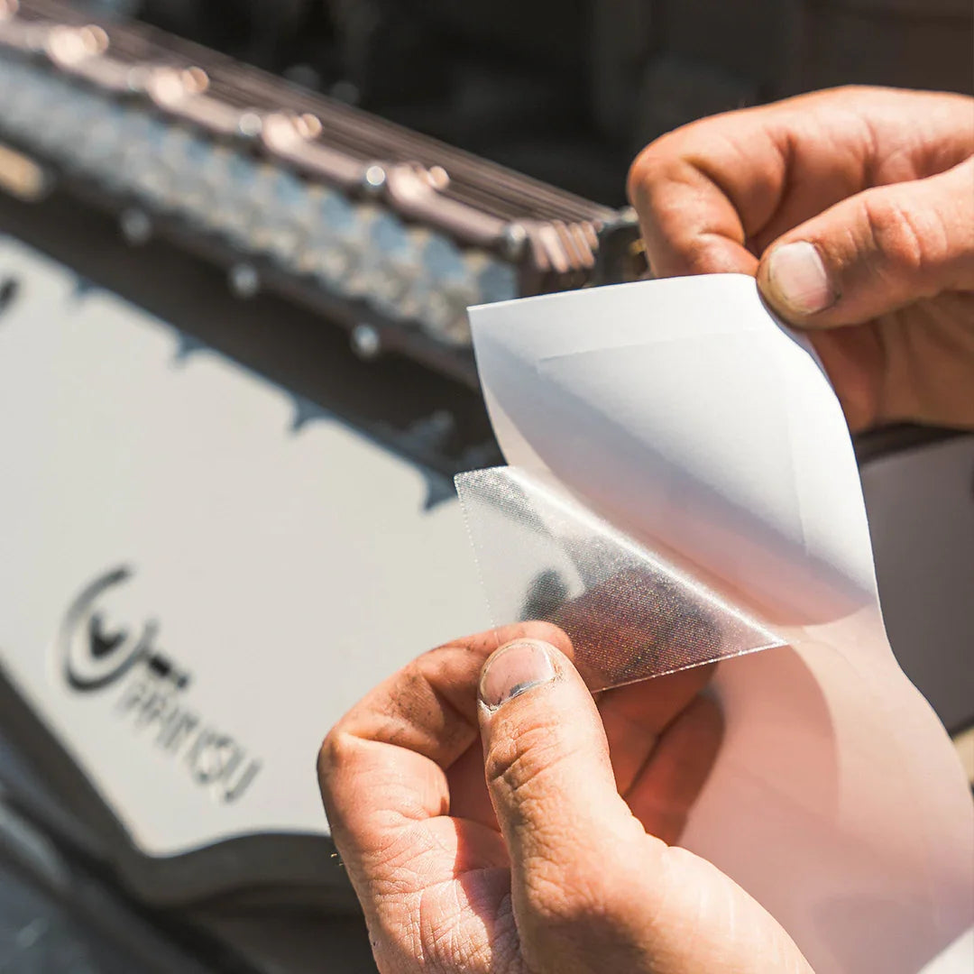 Hands applying clear protective film to off-road vehicle grille near LED light bar