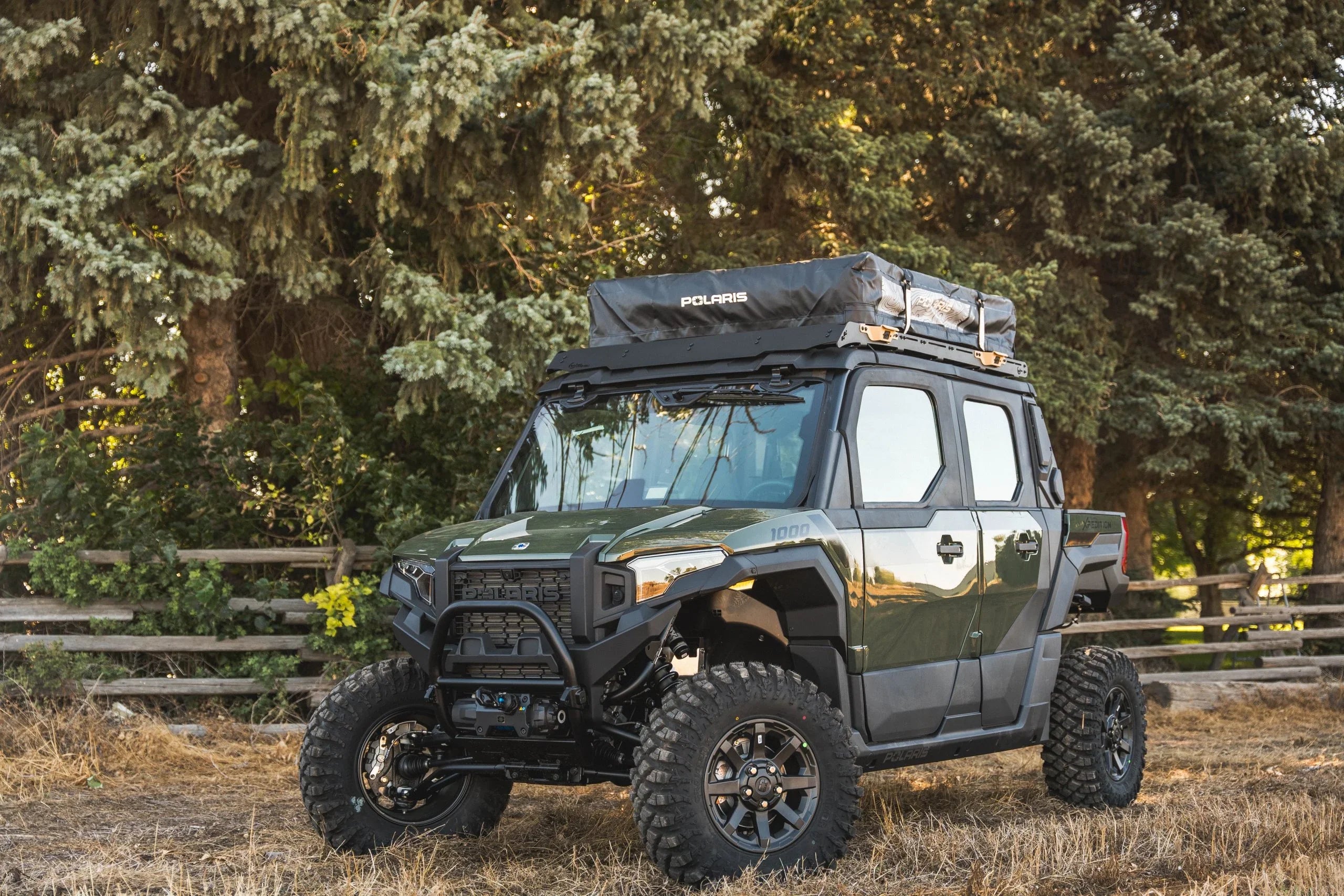 Polaris off-road adventure vehicle with rooftop tent parked outdoors in a forest setting