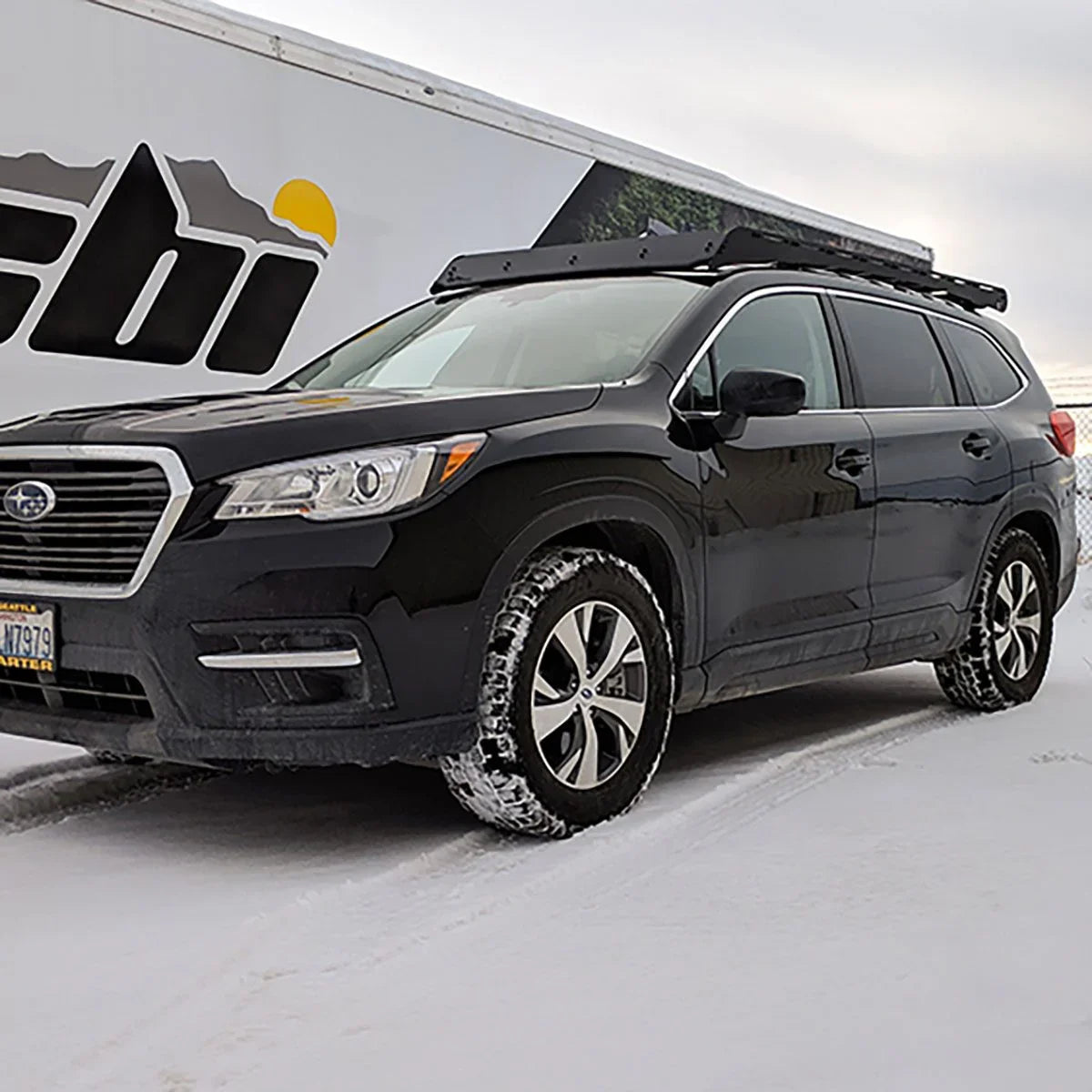 Black Subaru SUV with roof rack parked on snowy ground, ideal for overlanding and adventure gear.