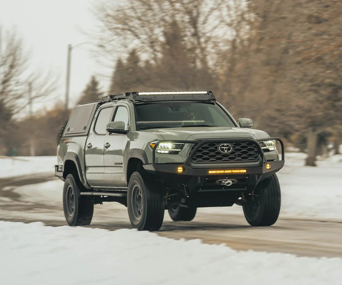 Toyota Tacoma with Prinsu cab rack driving on snowy road, off-road lighting visible