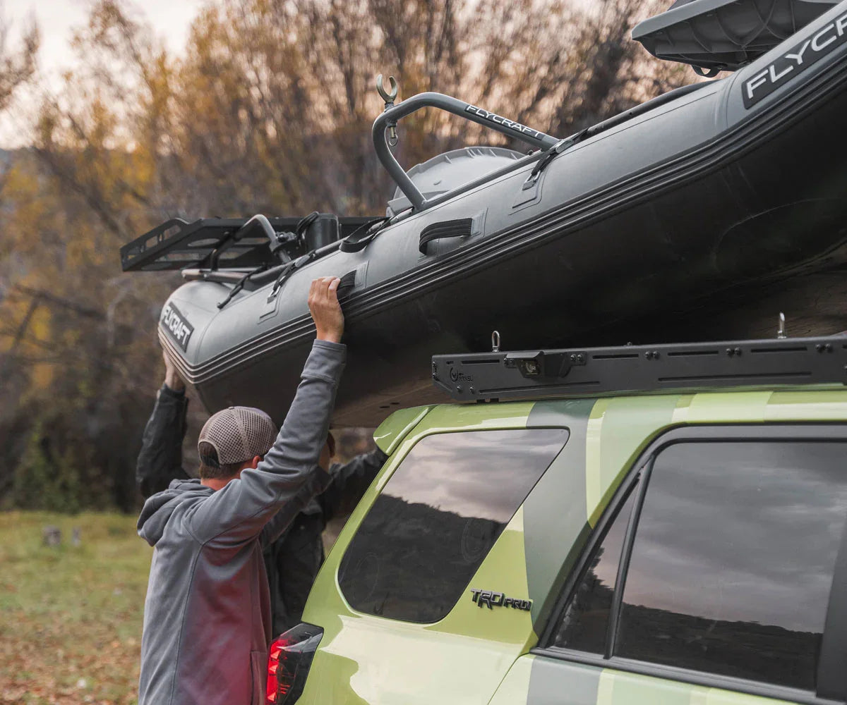 Man loading inflatable boat onto roof rack of Toyota 4Runner TRD Pro in outdoor setting