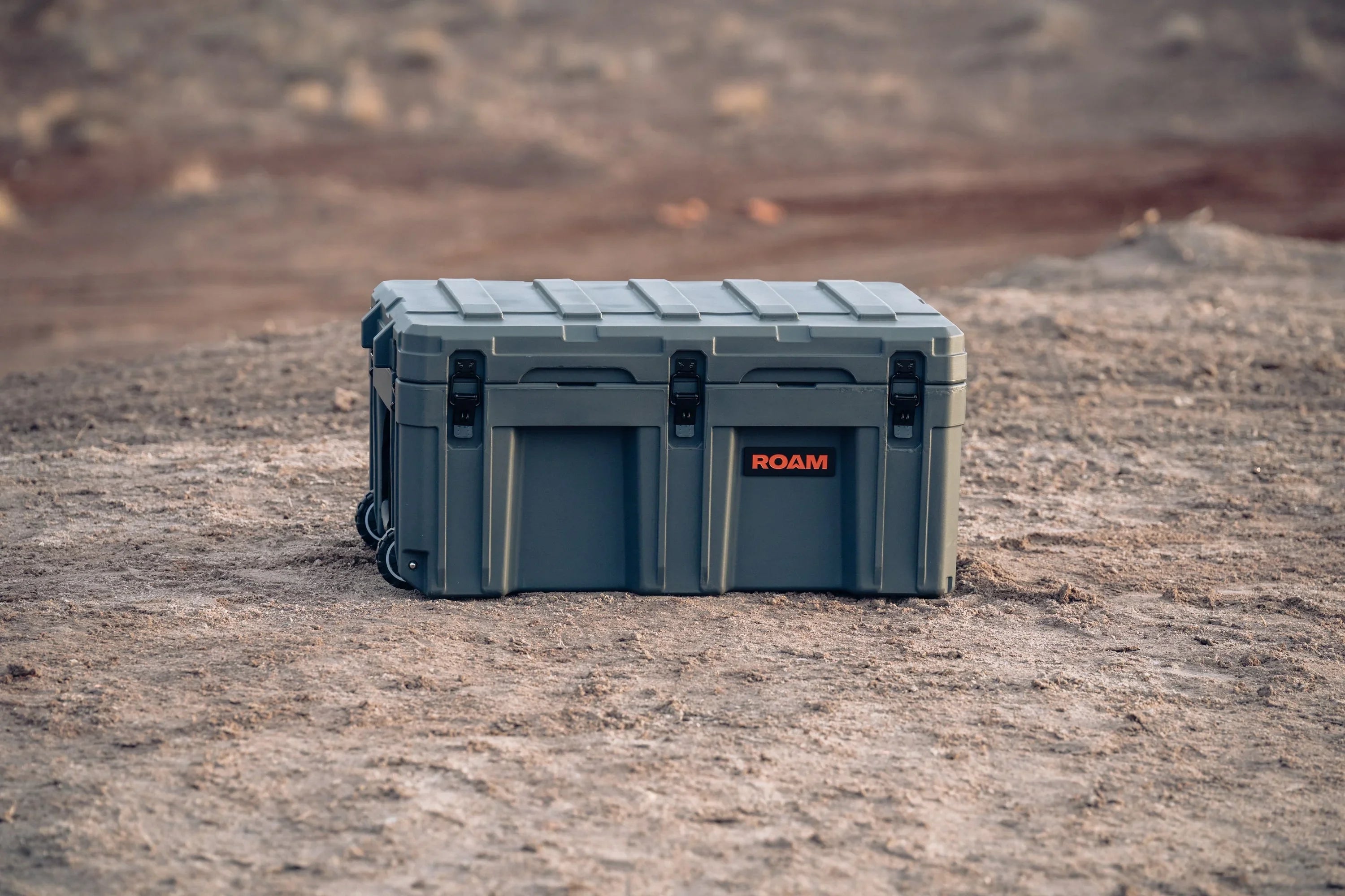 Rugged gray overland storage box with ROAM logo on desert terrain, outdoor camping gear