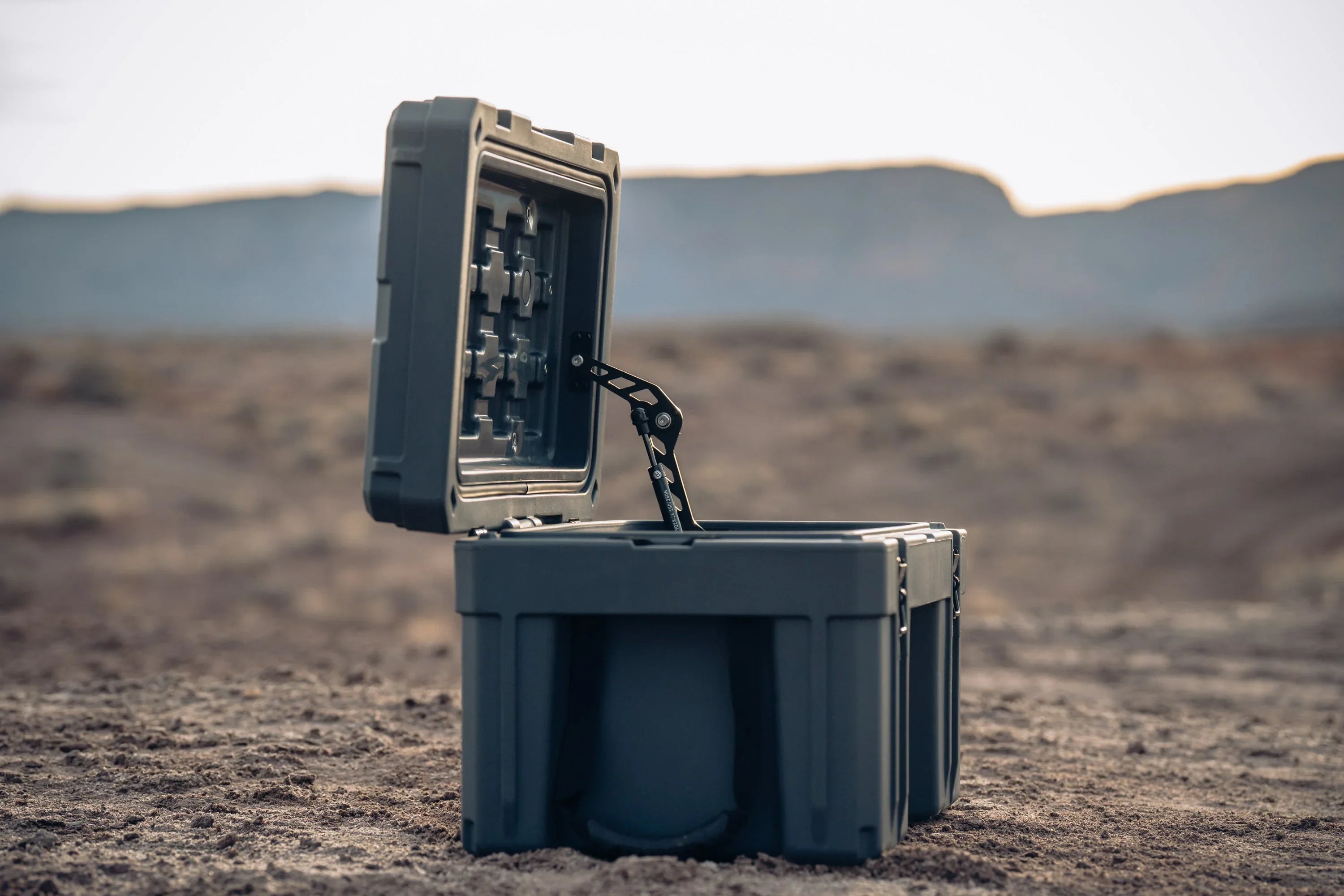 Heavy-duty camping storage box with open lid on rugged outdoor terrain