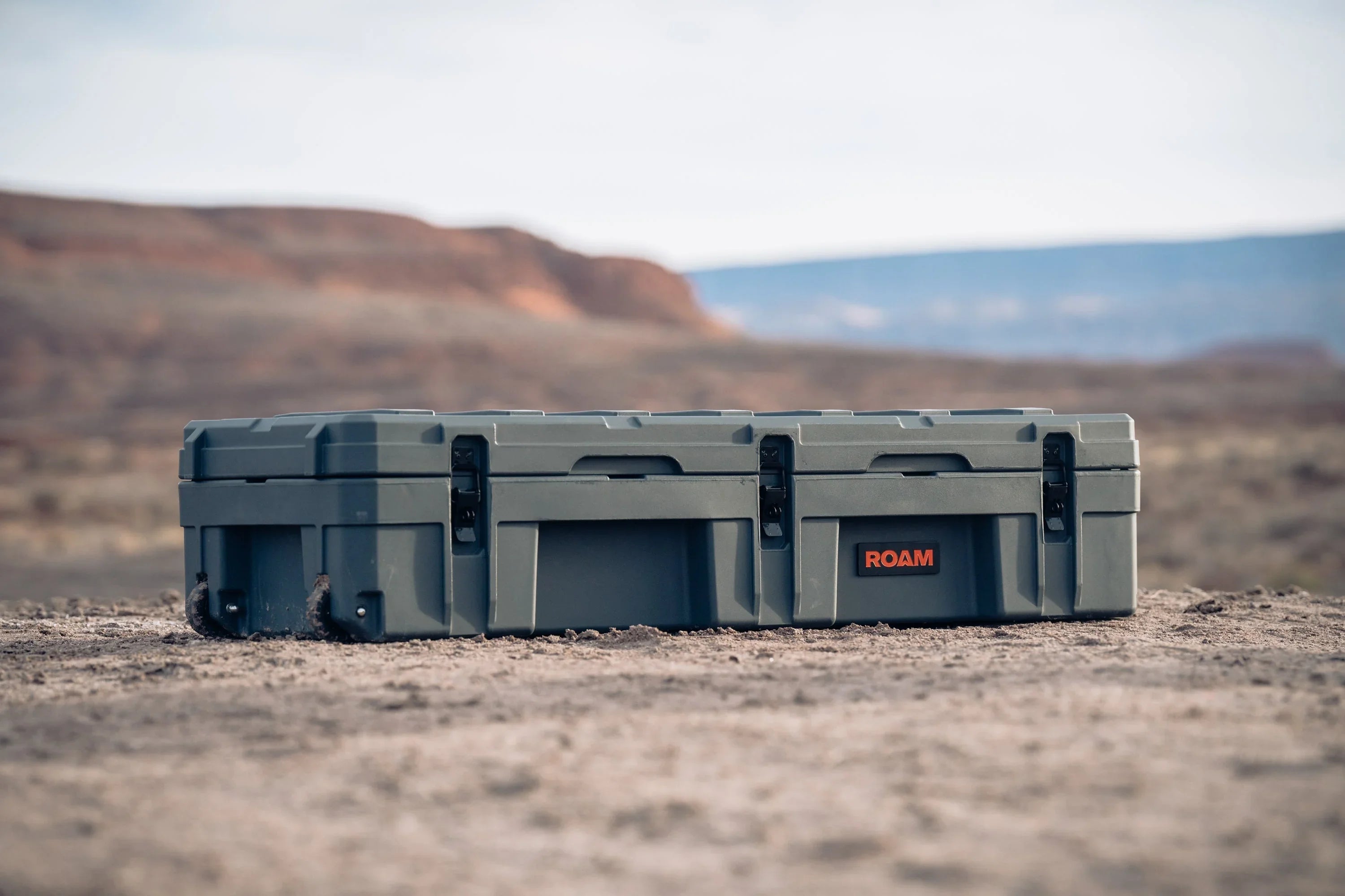 Overland gear storage case with ROAM logo on desert terrain, outdoor camping equipment