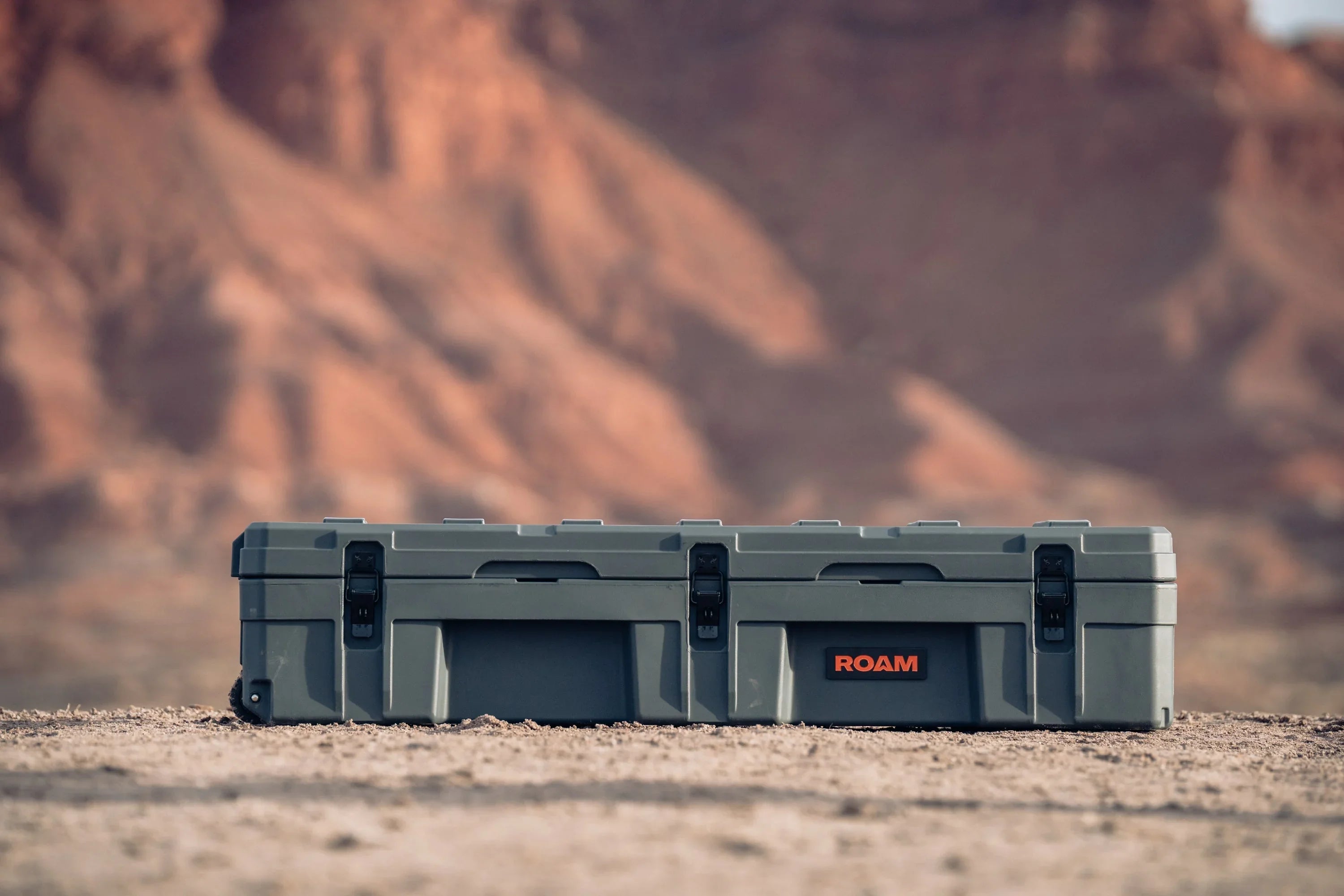 Heavy-duty grey camping storage case with black latches on rugged desert terrain