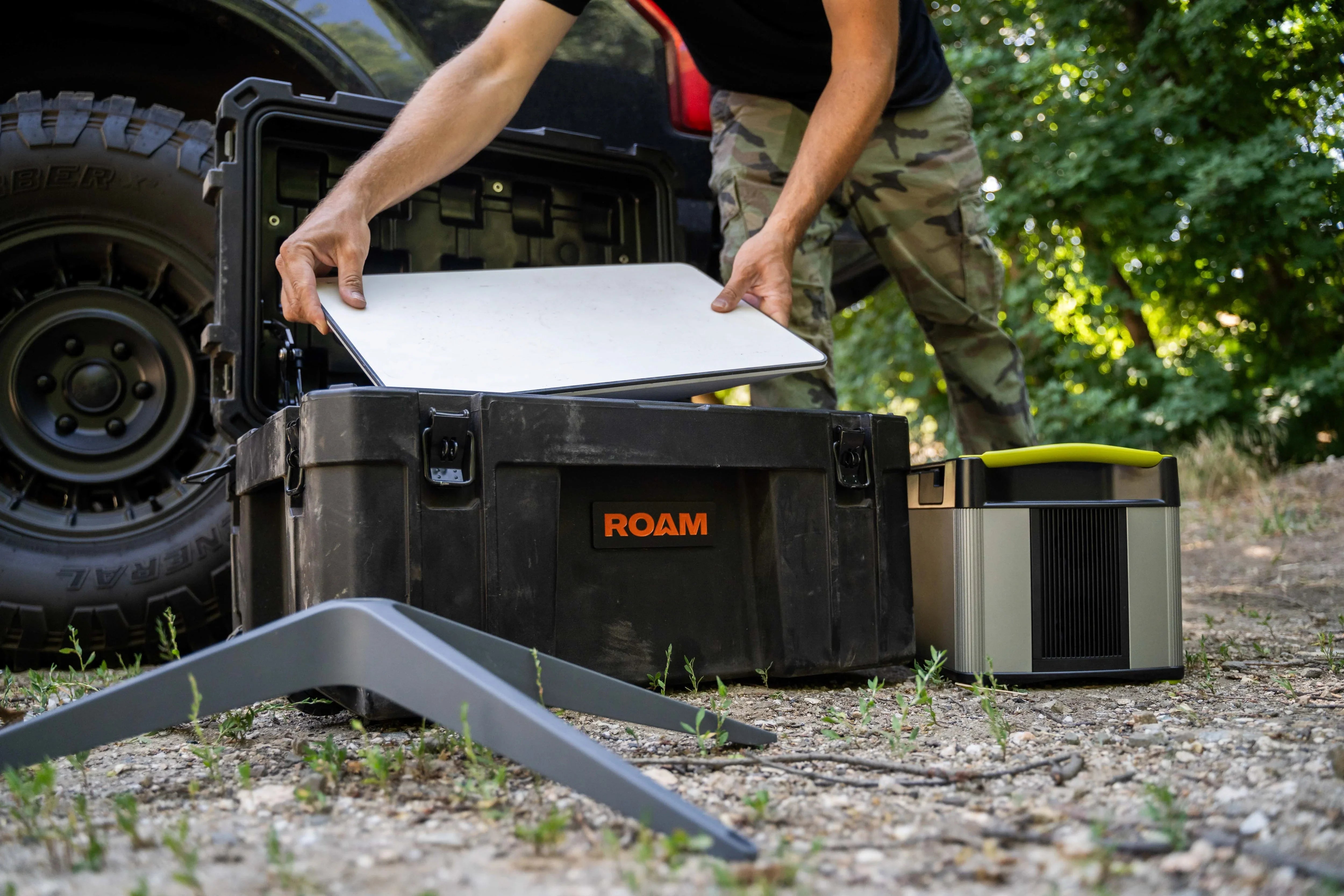 Man packing portable camping gear into a rugged black storage box outdoors near SUV tire