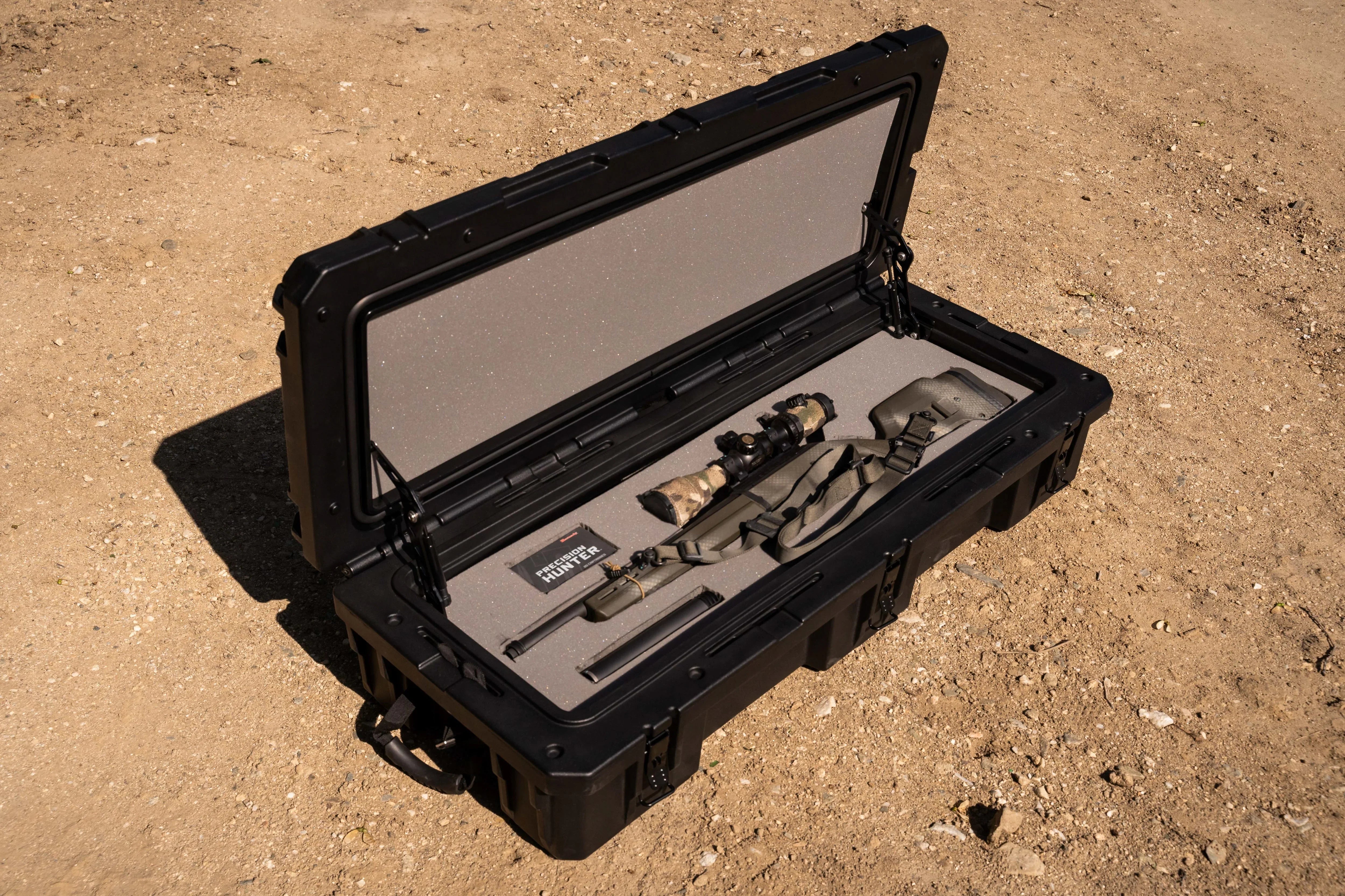 Hard rifle case with foam interior, rifle, and accessories on outdoor dirt ground