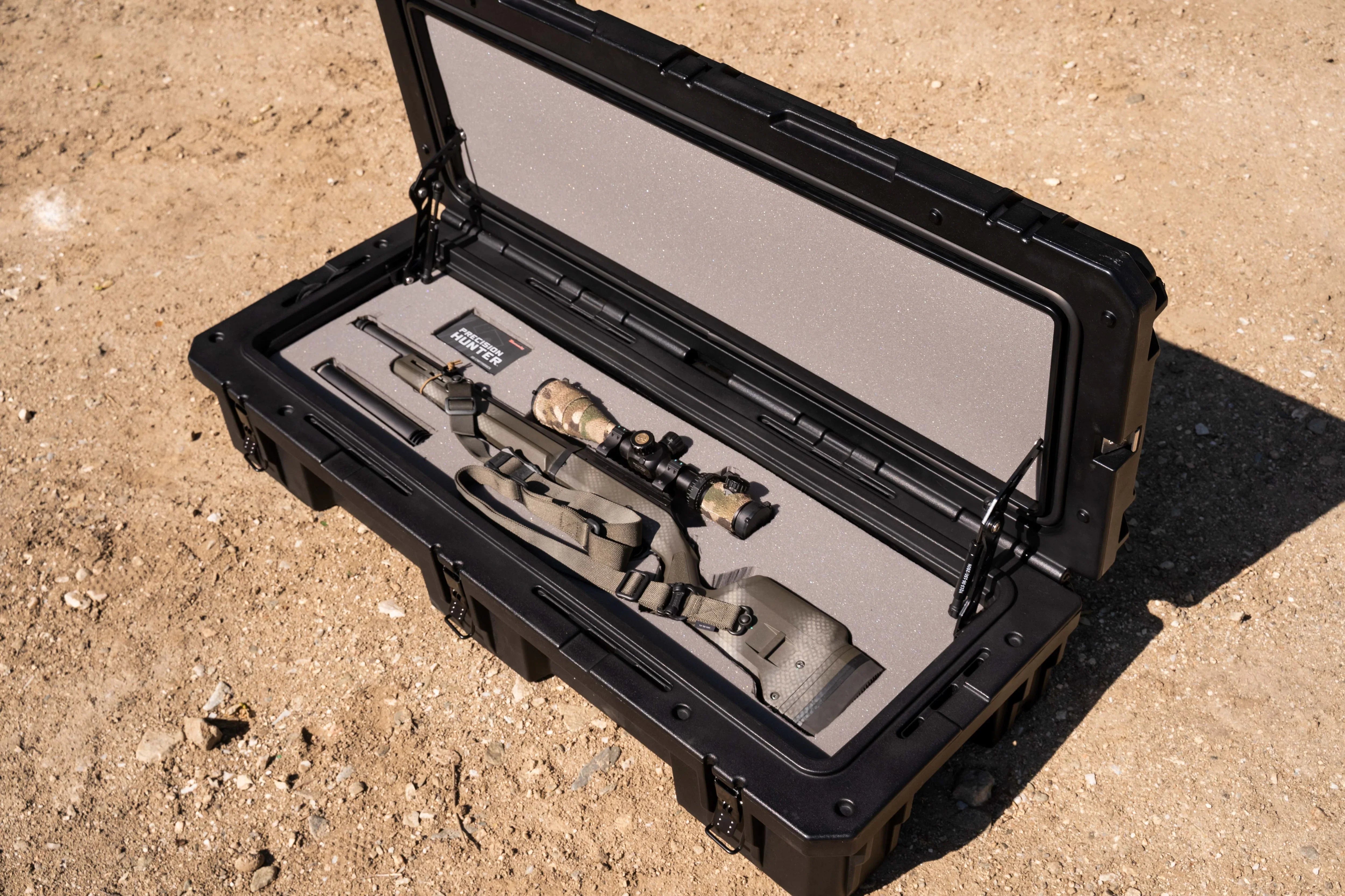 Rifle with camouflage scope in black hard protective case on outdoor dirt ground