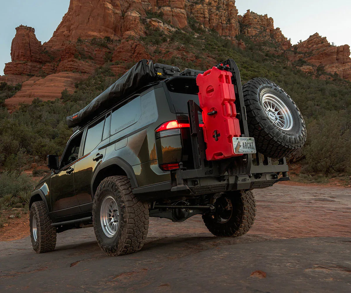 Lifted SUV with off-road tires, roof tent, spare tire and fuel can in rocky desert landscape