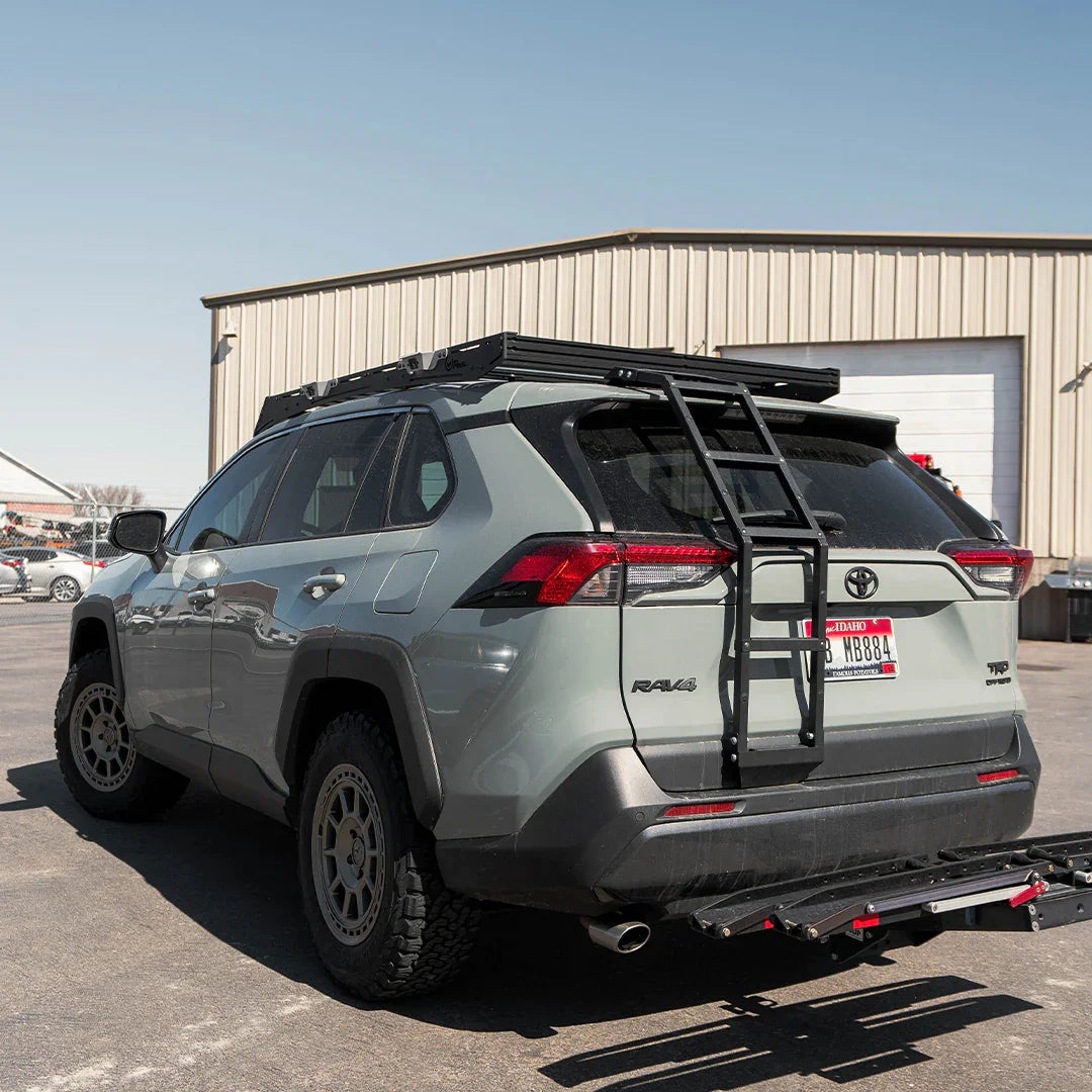 Toyota RAV4 with off-road tires, roof rack, and rear ladder in parking lot