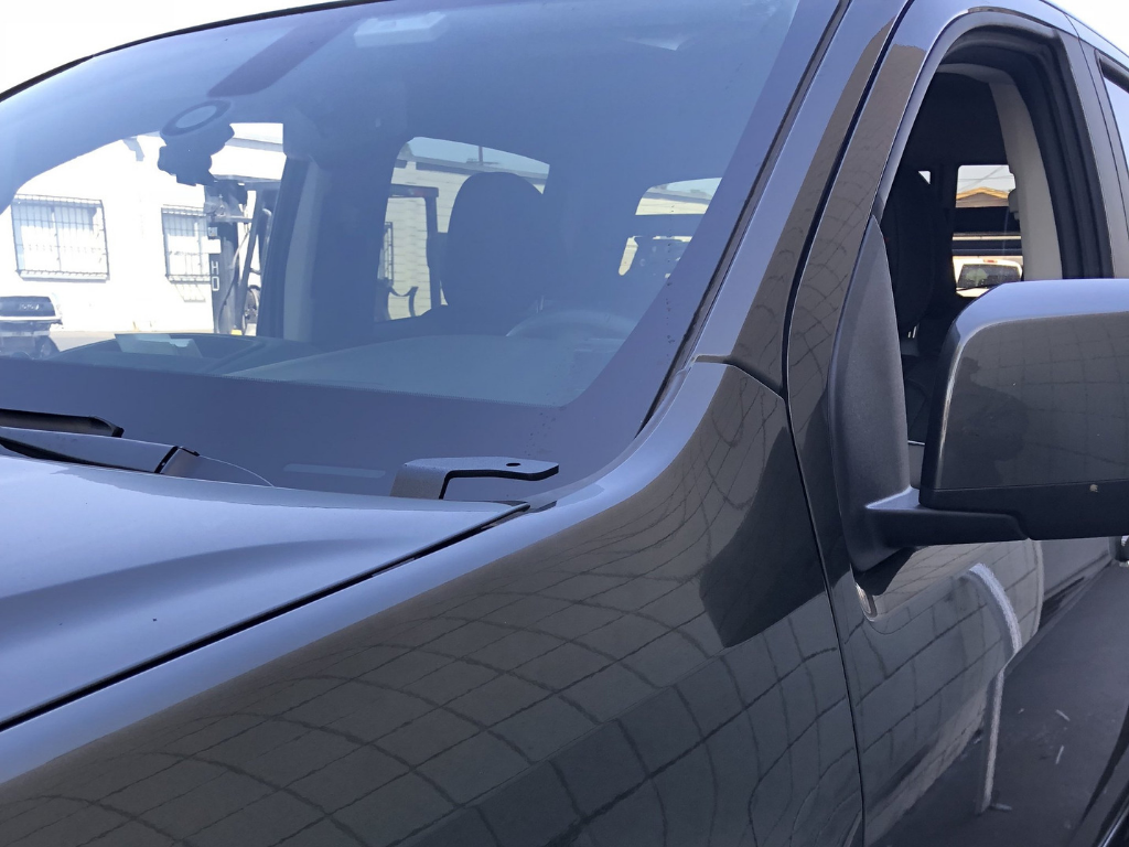 Close-up of a Toyota Tacoma windshield, side mirror, and hood in outdoor setting
