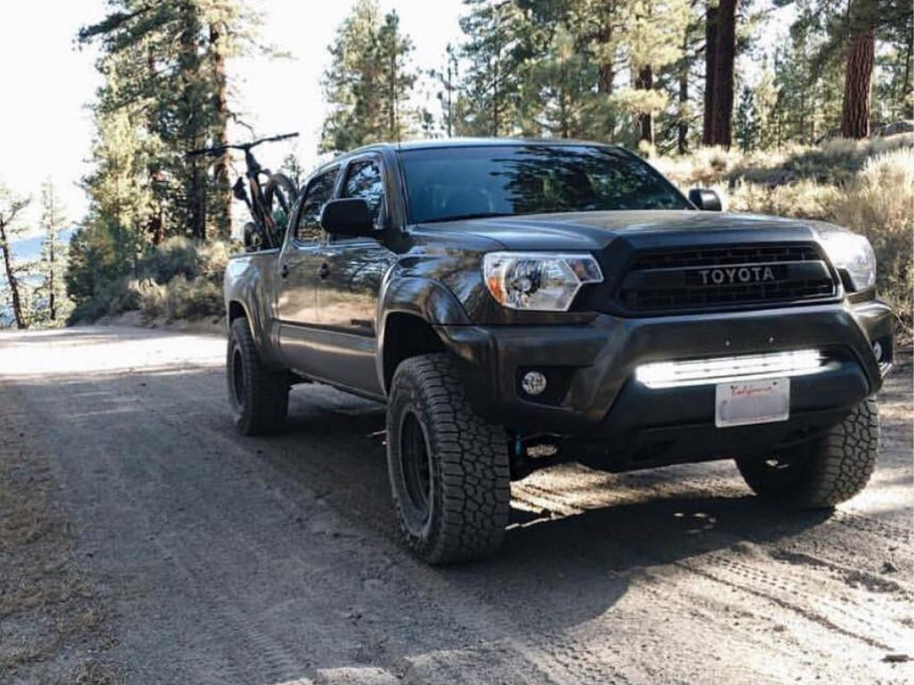 Toyota Tacoma overlanding truck with off-road tires and bike rack on a forest trail