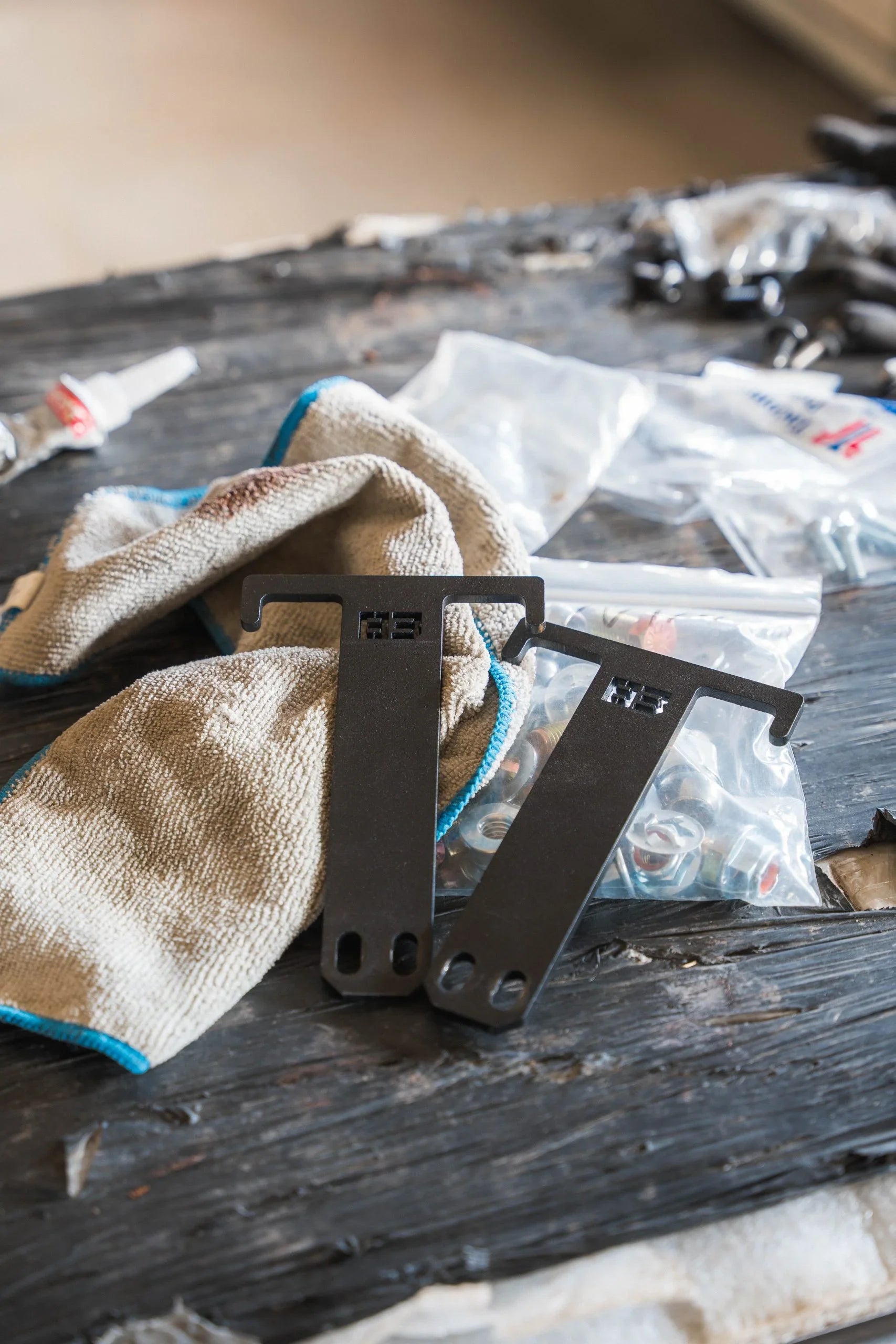 Two metal case mounts for vehicle accessories on workshop table with bolts and cloth.