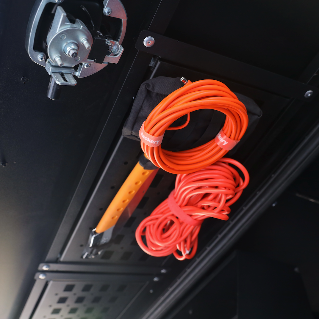 Overlanding vehicle storage system with orange extension cords and a mounted tool