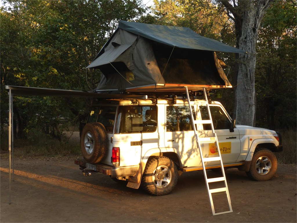 Overland vehicle with rooftop tent and side awning set up for camping in a forest