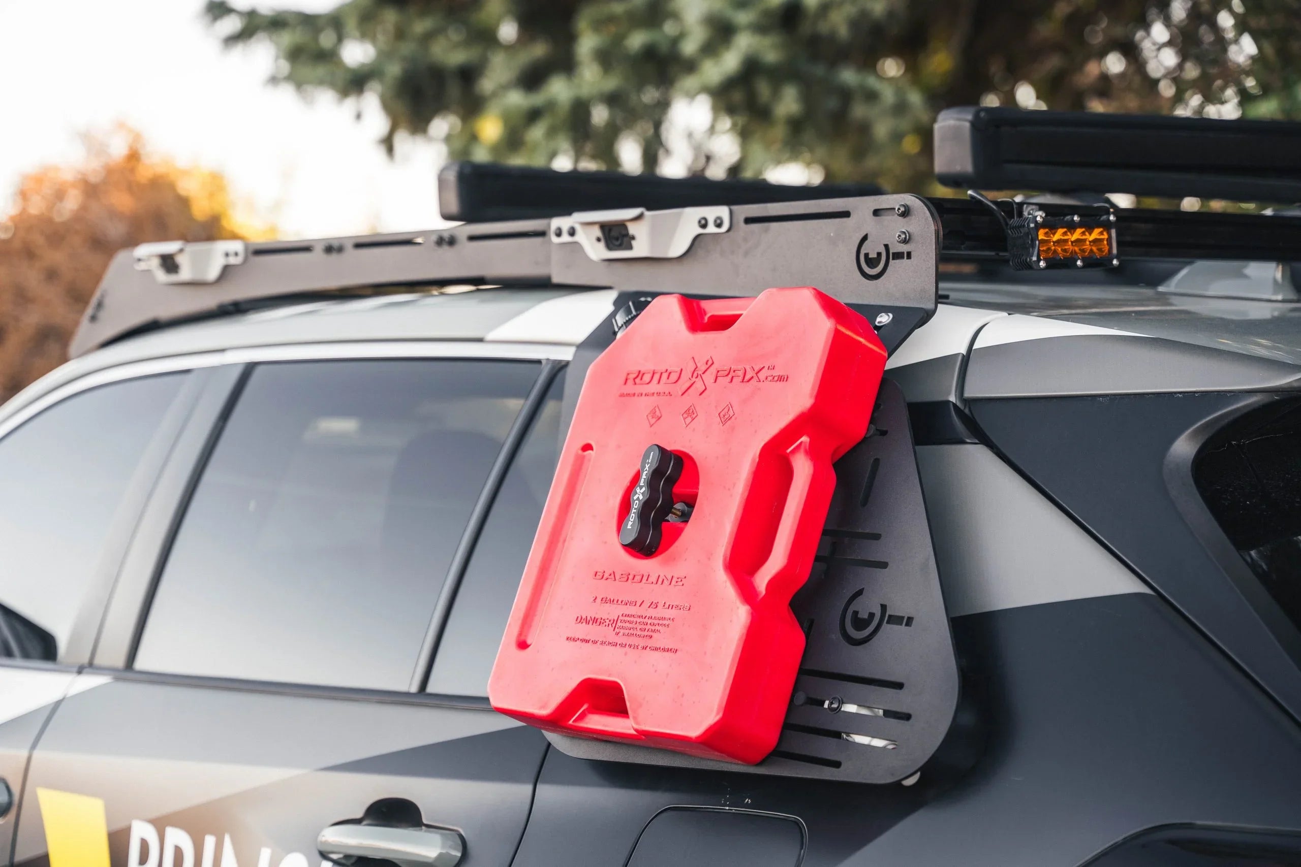 Red RotopaX fuel can mounted on off-road SUV side panel with roof rack and accessory light.