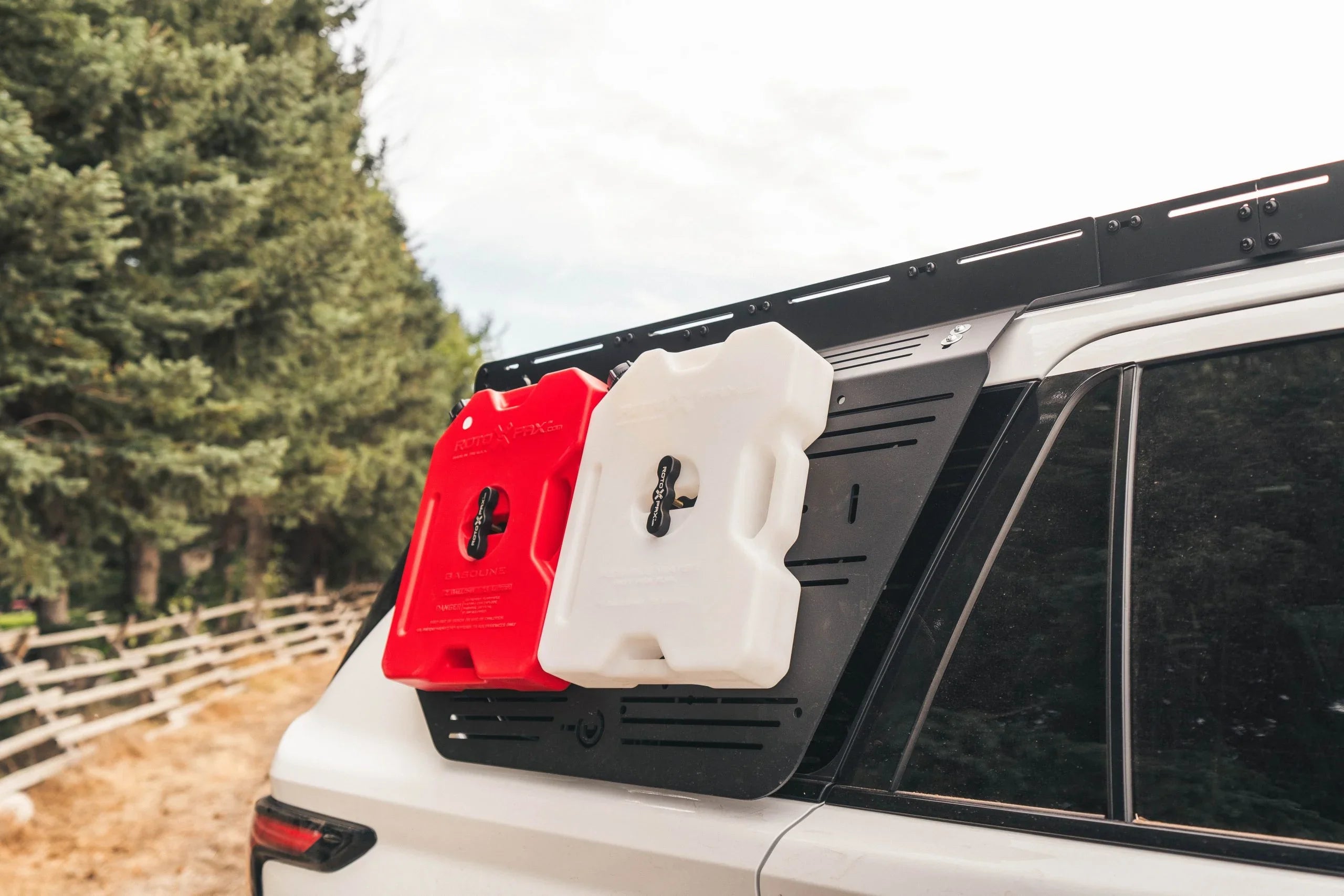 Overland vehicle side panel with red and white fuel and water containers, outdoor setting