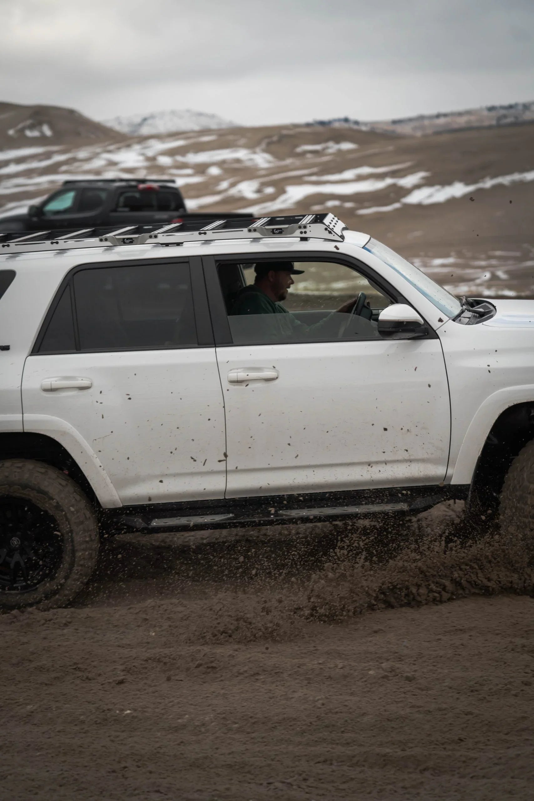 Toyota 4Runner with roof rack driving off-road on muddy terrain with snow-covered hills