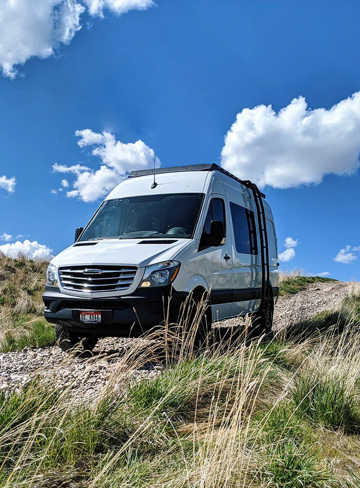 Sprinter van with roof rack on an off-road trail in grassy outdoor landscape