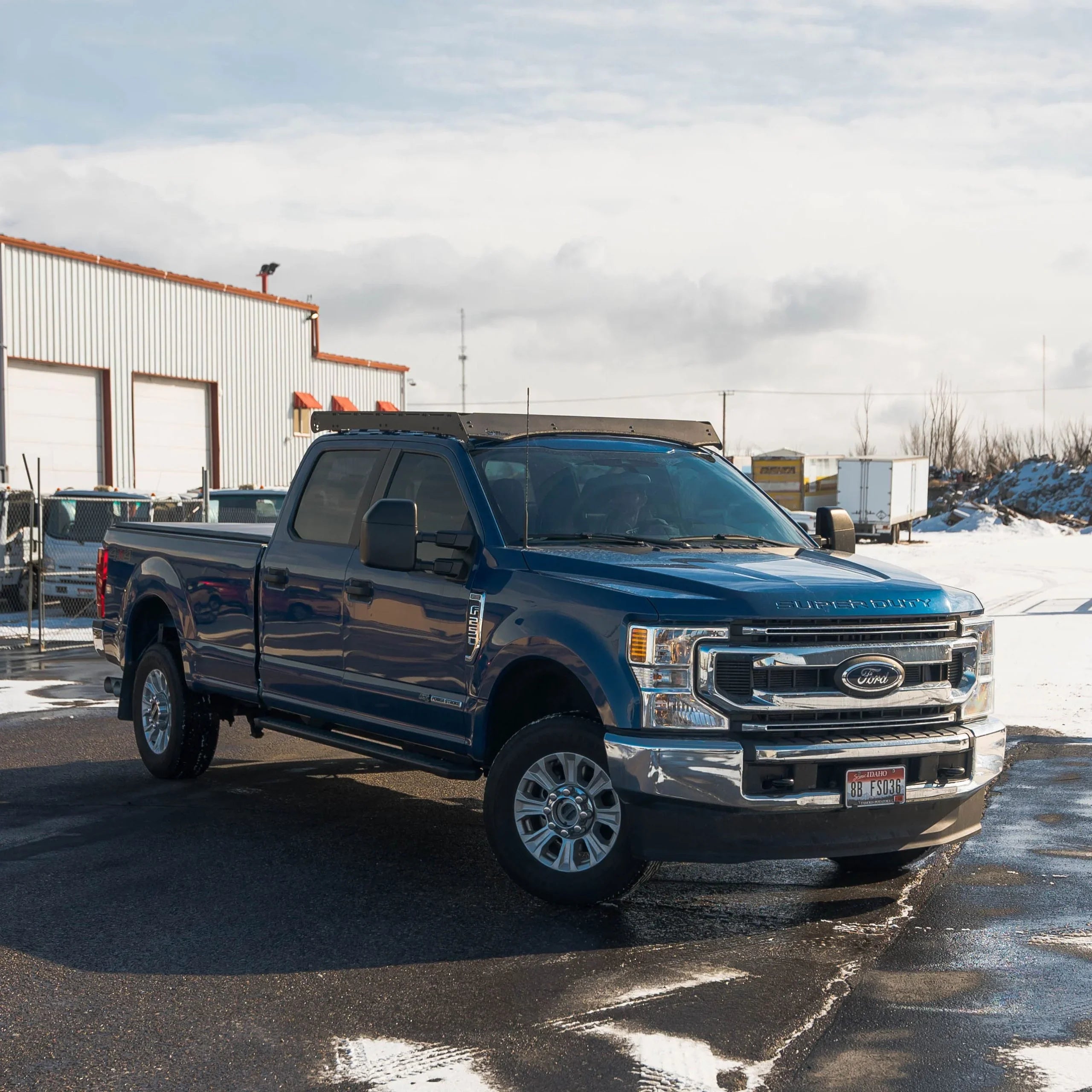 Blue Ford Super Duty truck with overland accessories parked on wet pavement in snowy lot