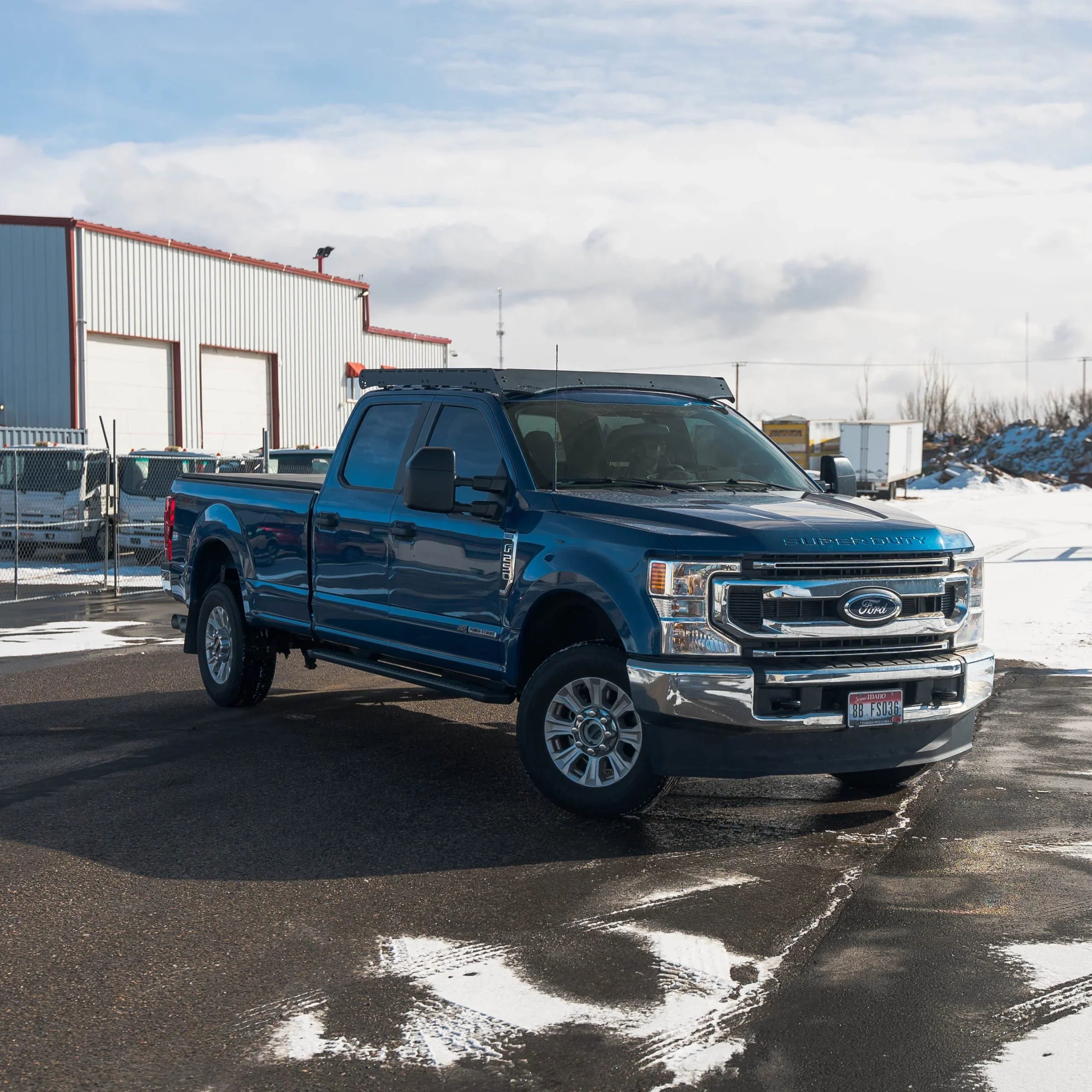 Blue Ford Super Duty truck parked outdoors near industrial warehouse, snow in background.